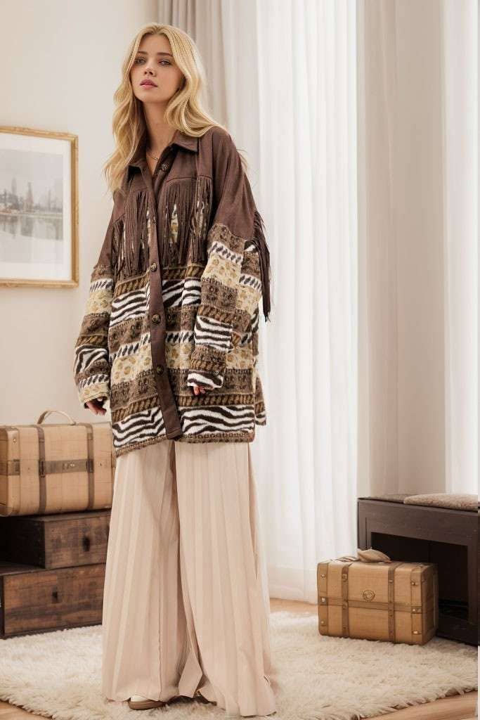 Brown Aztec print shacket with fringe detail, button closure, and patterned sleeves, styled with cream pleated pants while seated on a sofa.