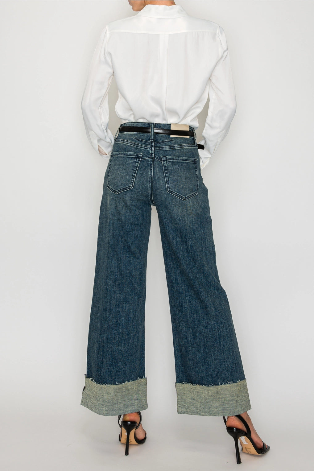 Back view — dark-wash high-rise wide-leg jeans with oversized cuffed hems, raw edge, classic back pockets on model.