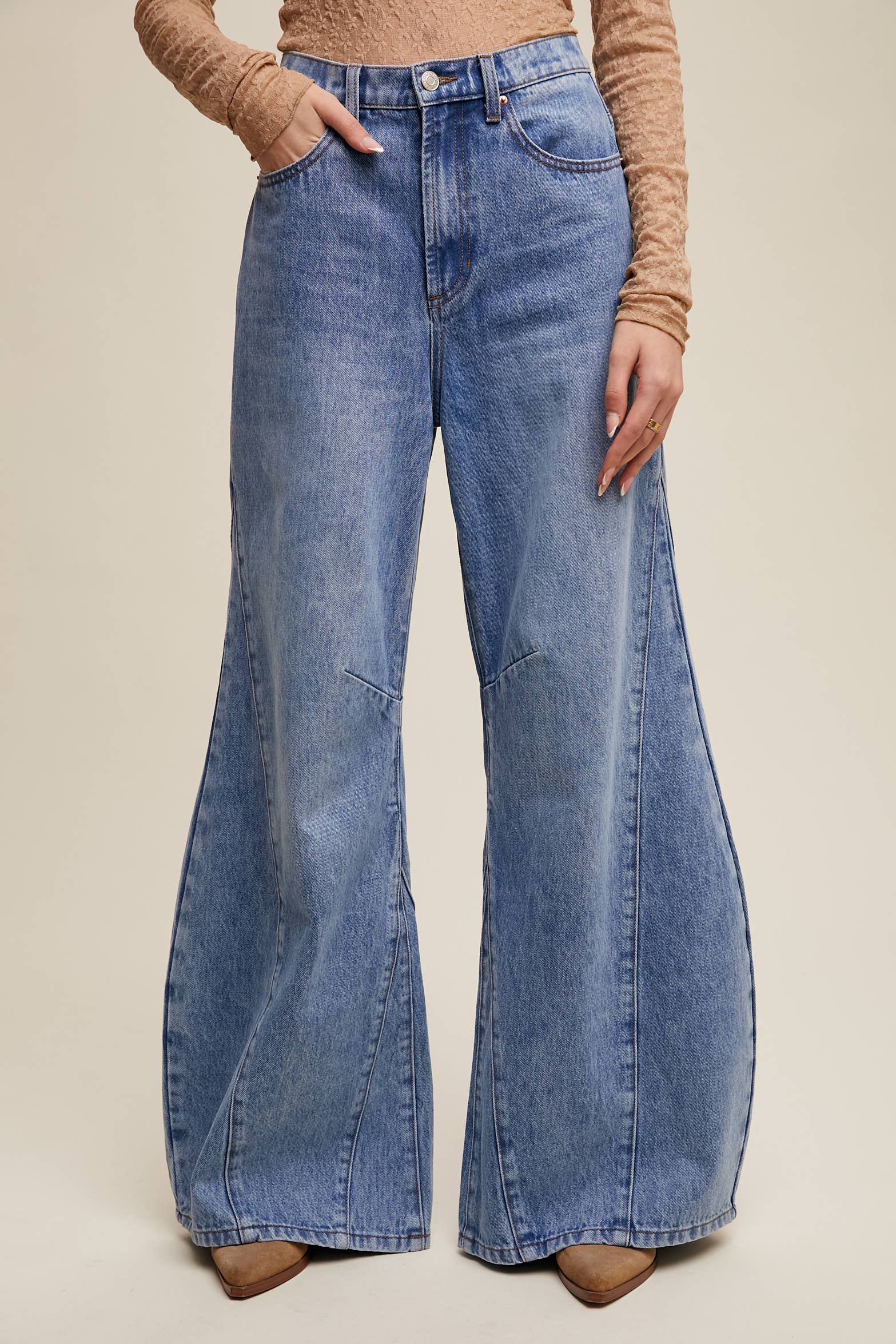 High-rise light-wash wide-leg jeans with front seam panels and knee darts, five-pocket style with zip fly, styled with tan long-sleeve top and pointed-toe boots.