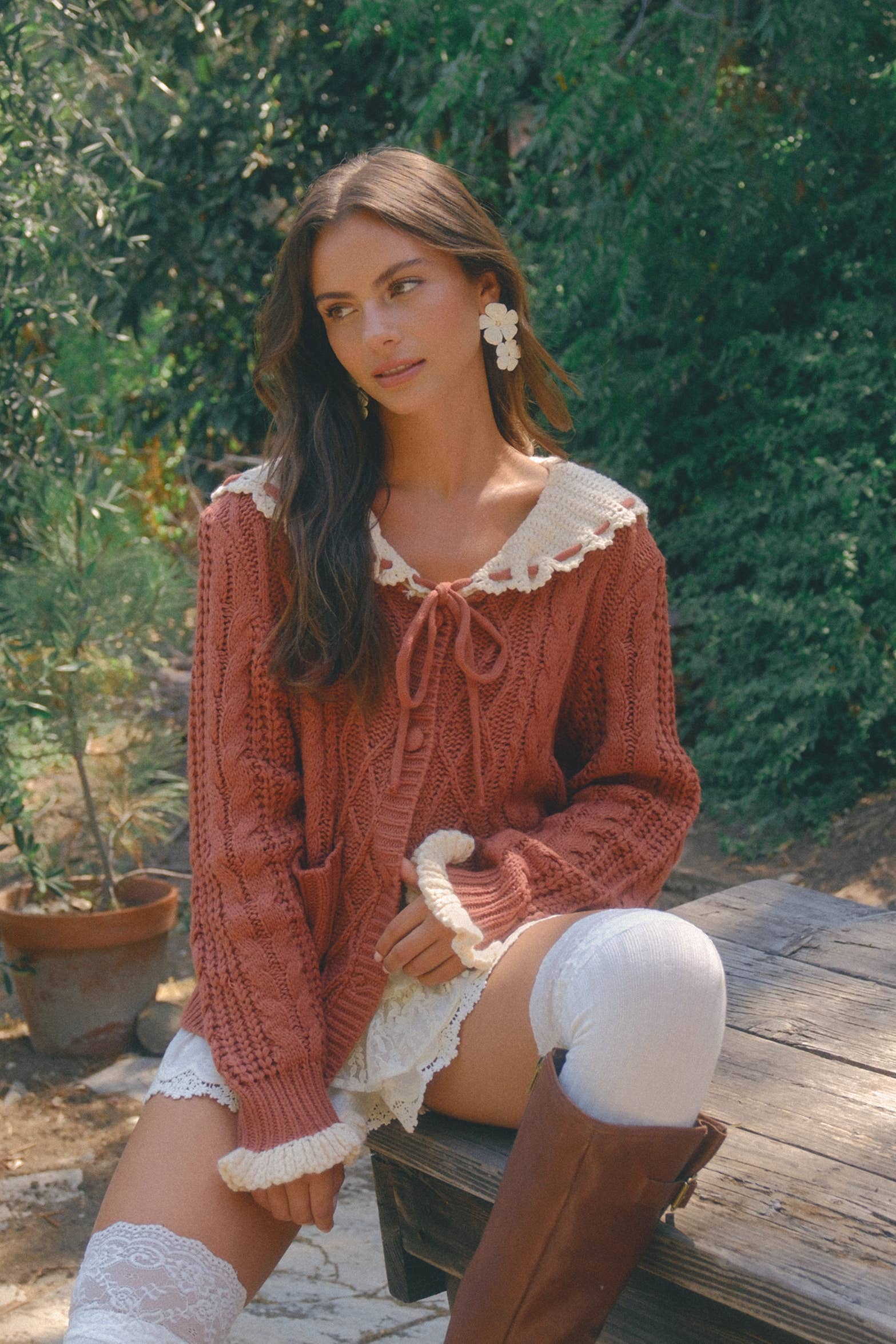 Woman in a cozy outfit with a knit cardigan and lace details sitting outdoors.