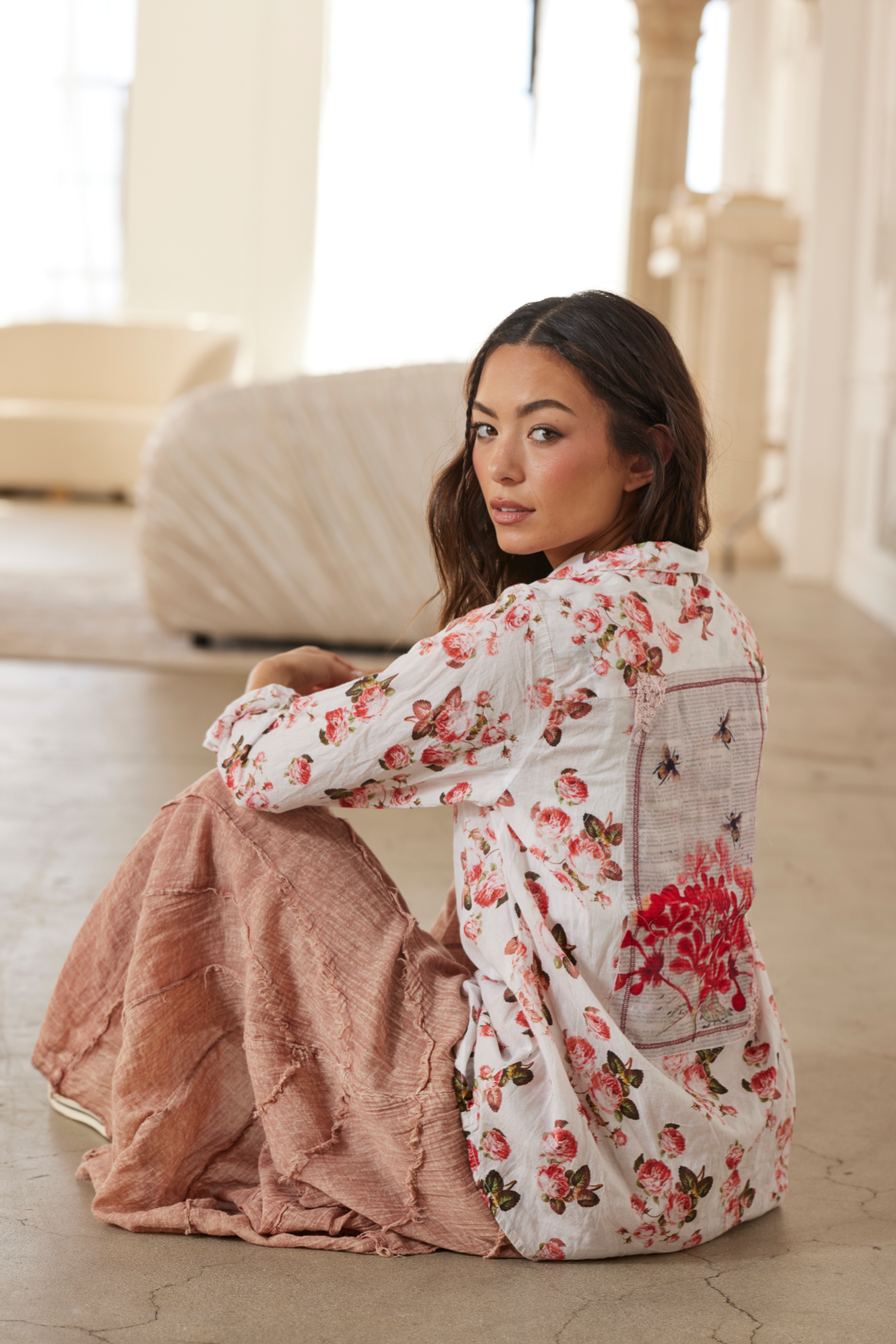 Woman sitting on a couch wearing a floral dress in a bright room.