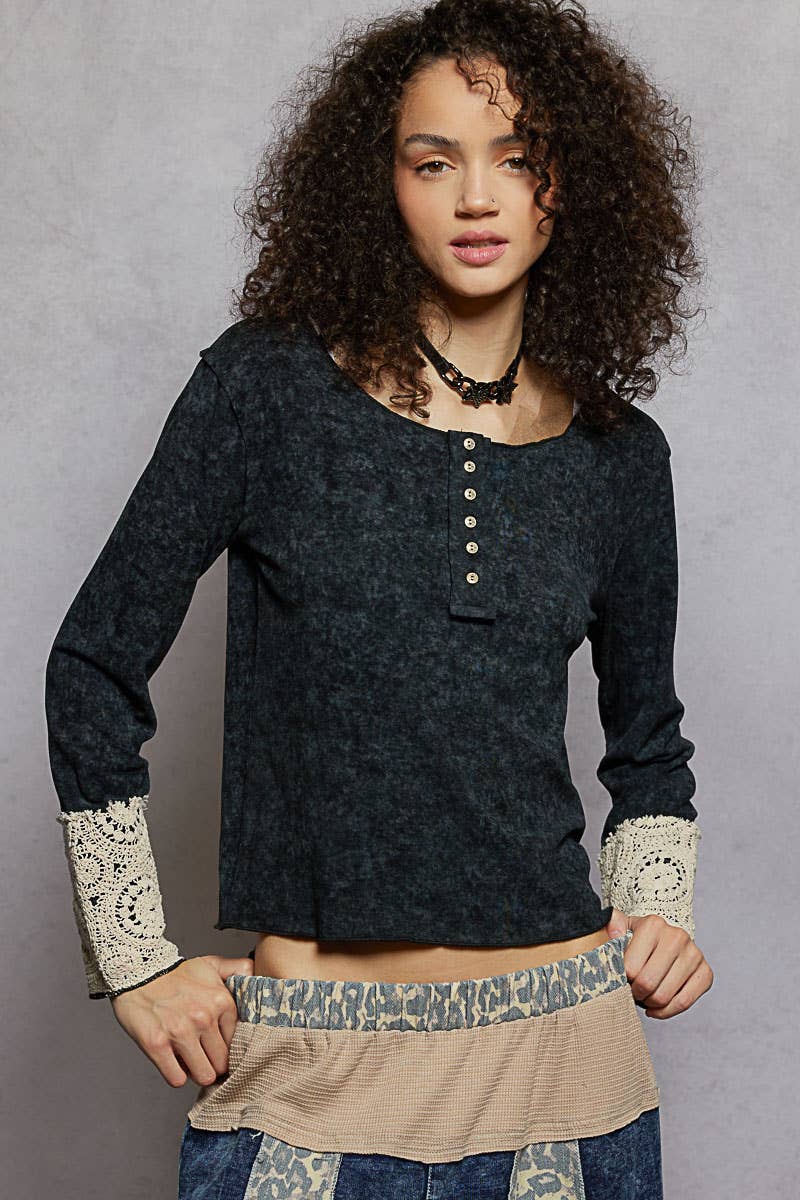 Woman wearing a dark blue long-sleeve top with lace cuffs against a gray background