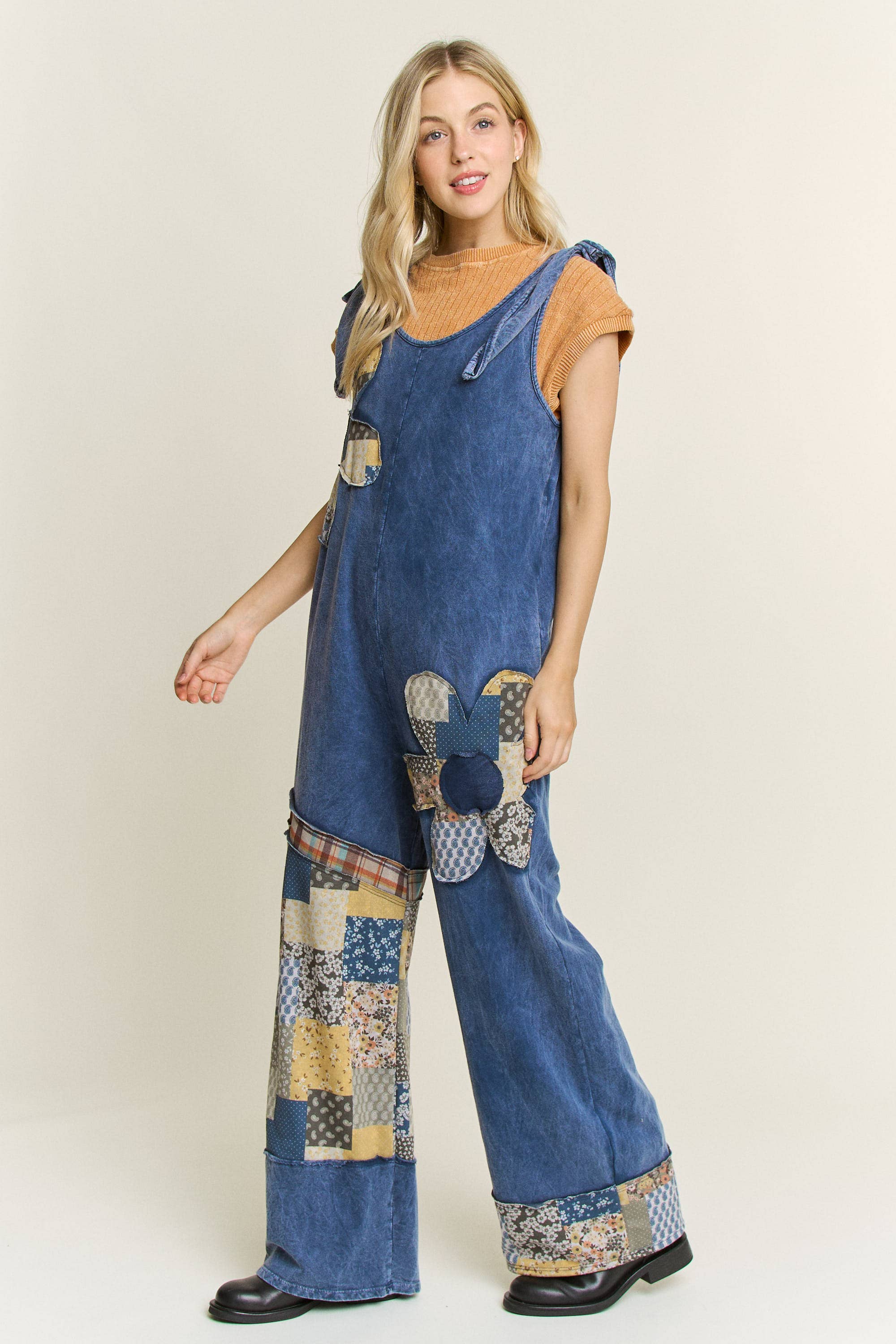 Woman wearing boho patchwork navy mineral-wash jumpsuit with daisy appliqués and wide legs. 