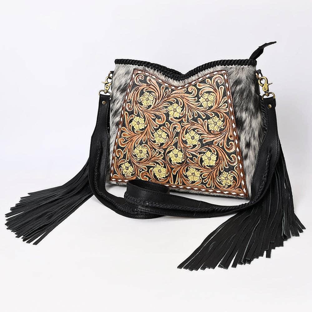 Handbag with floral tooled leather design and black fringe on a white background