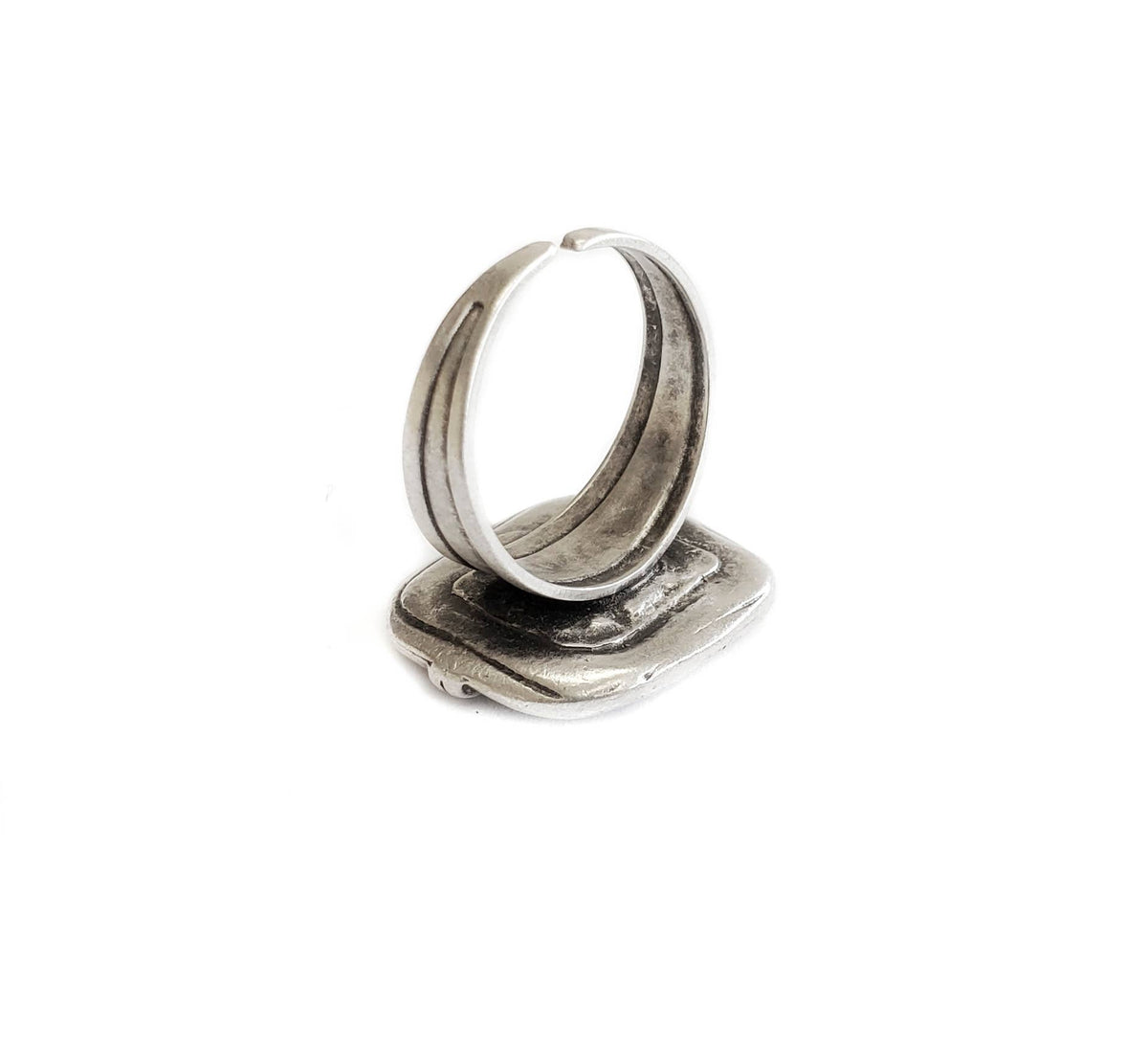 A rustic silver ring with a textured, antique finish, standing upright on its flat rectangular base against a solid white background.