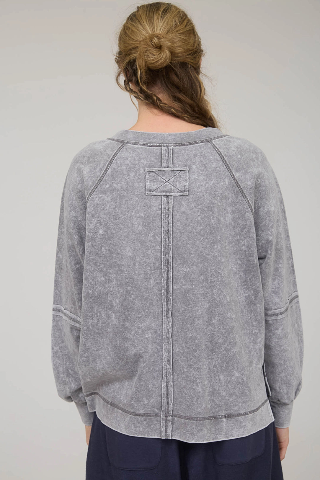 Person wearing a gray sweatshirt with a logo on the back against a plain background