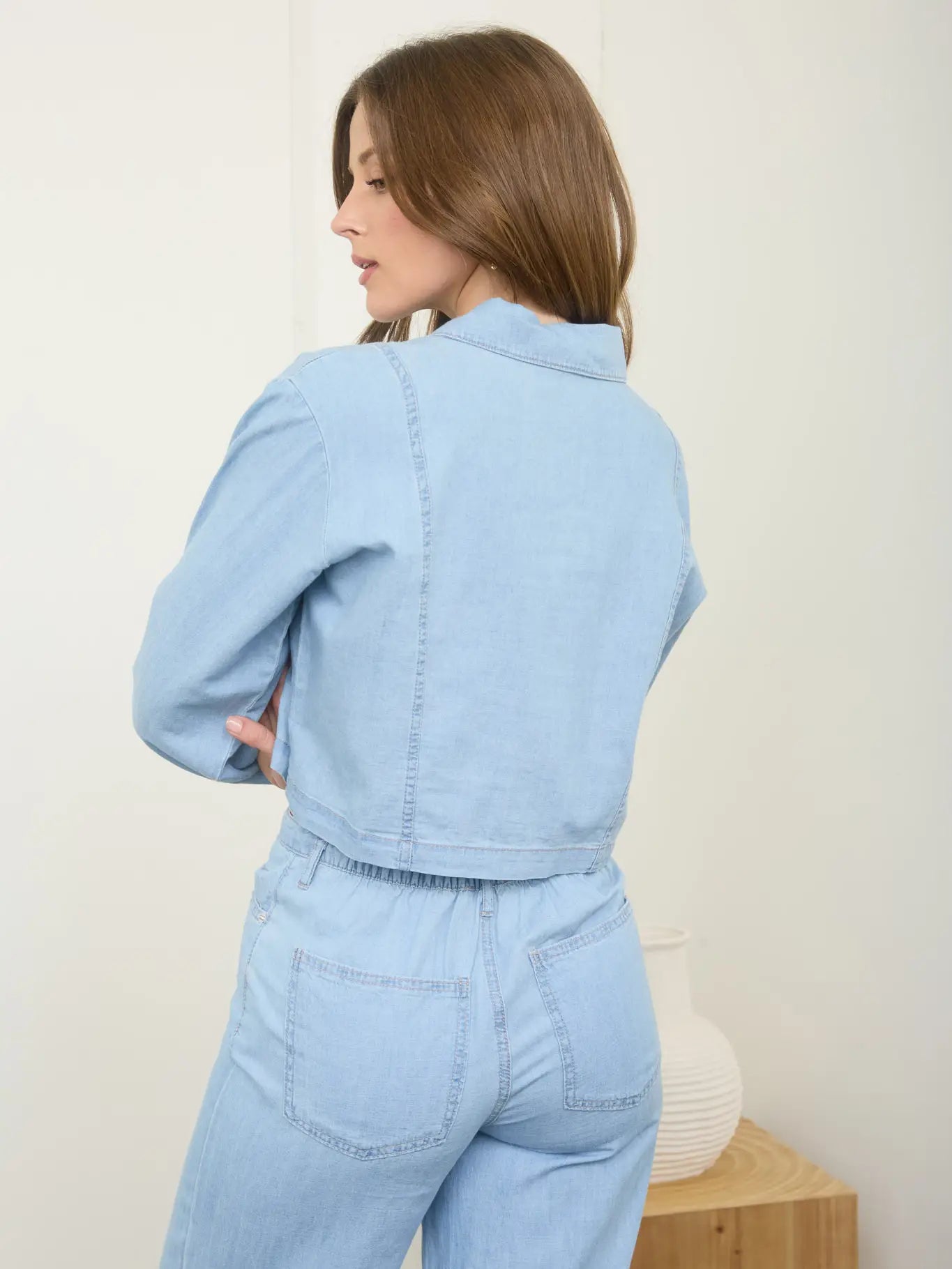 Woman wearing a light blue denim outfit standing against a white background