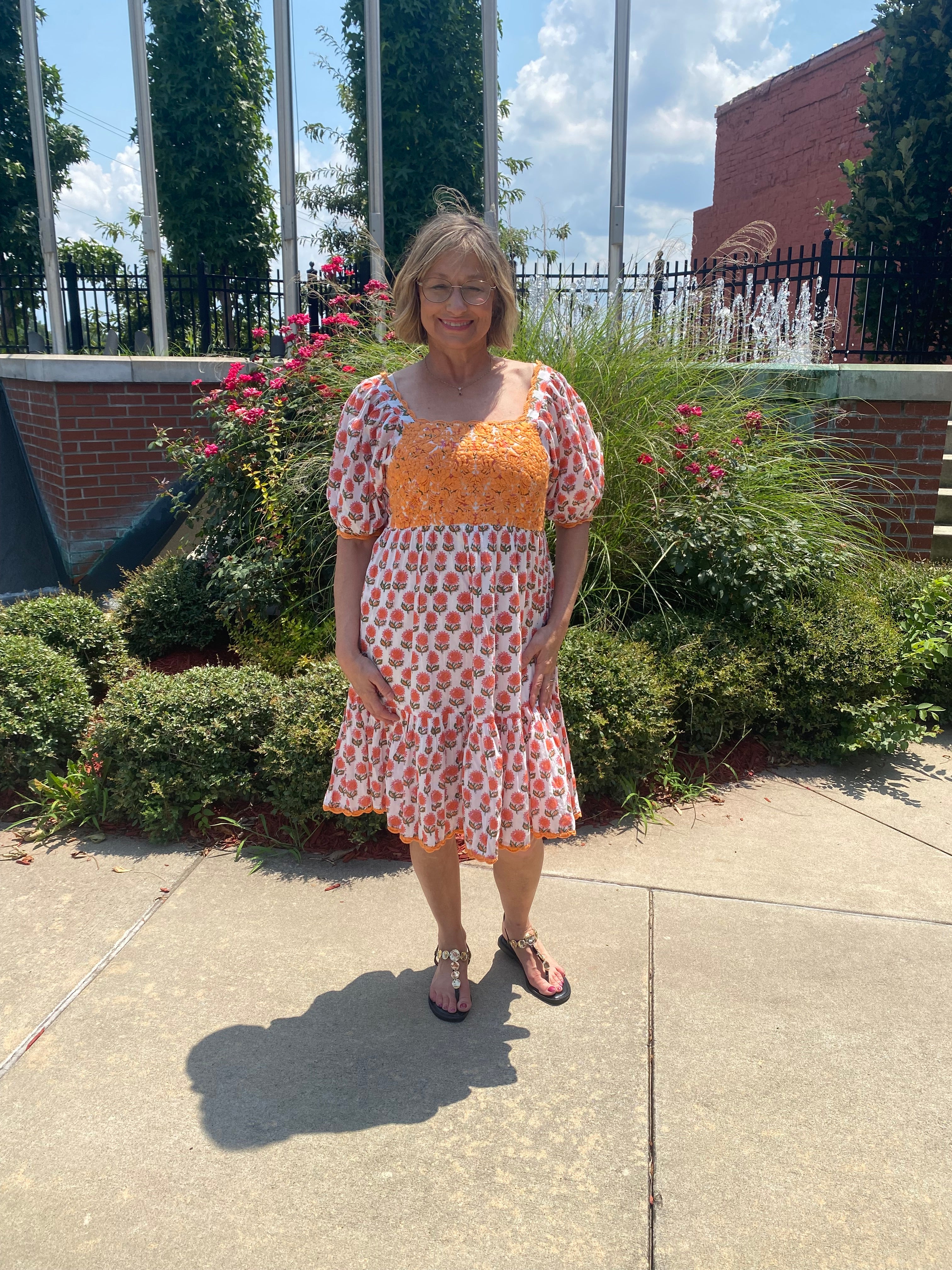 Orange crochet bodice, pink floral block print tiered skirt, puff sleeves, styled with sandals outdoors