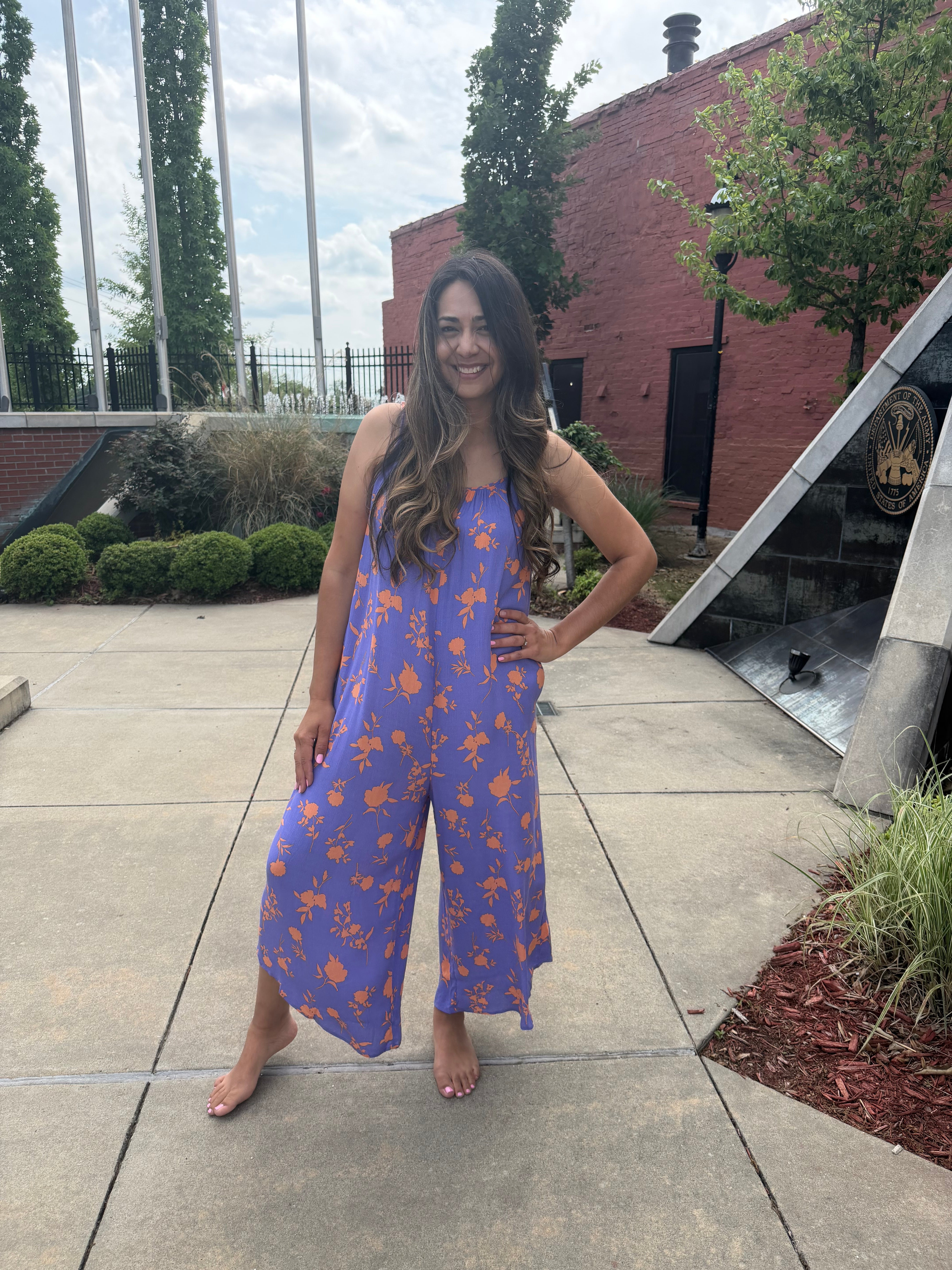Woman in a blue floral dress standing on a sidewalk with trees and a building in the background