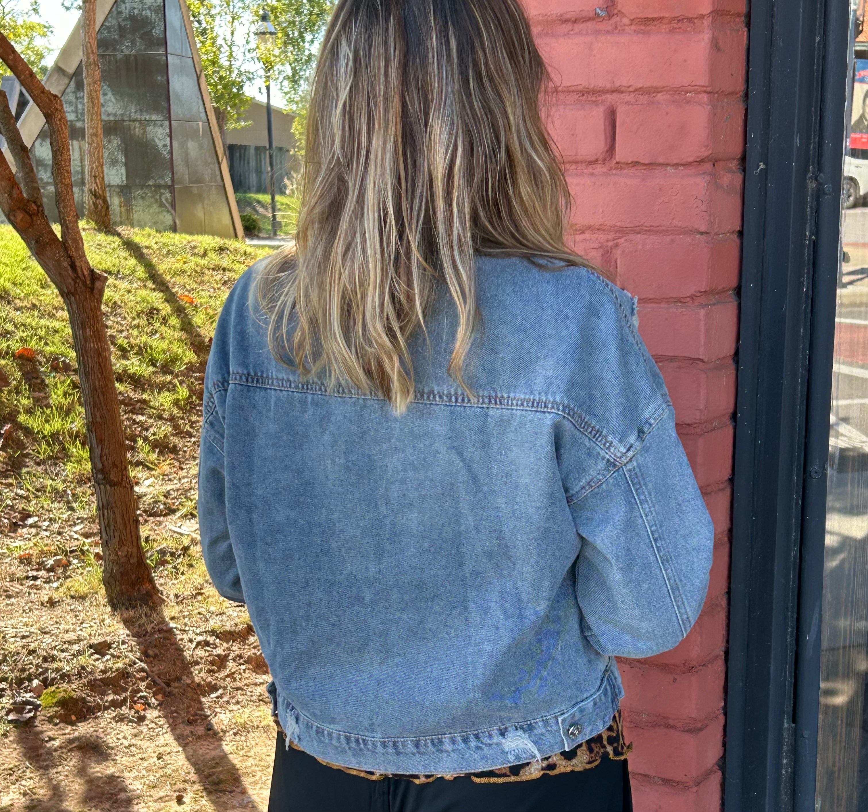 Person wearing a denim jacket standing next to a brick wall outdoors