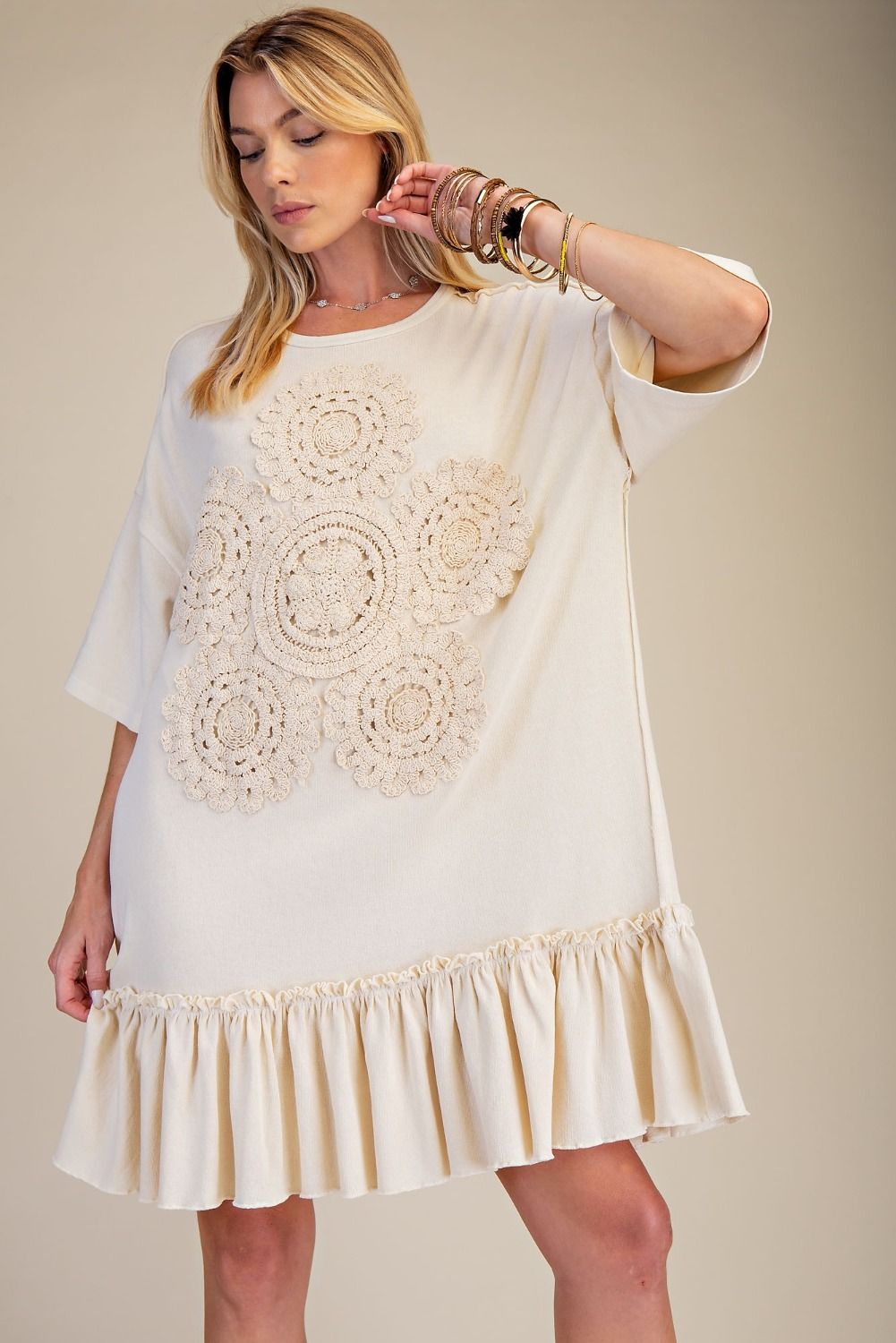 Woman wearing a white dress with crochet detailing on a beige background