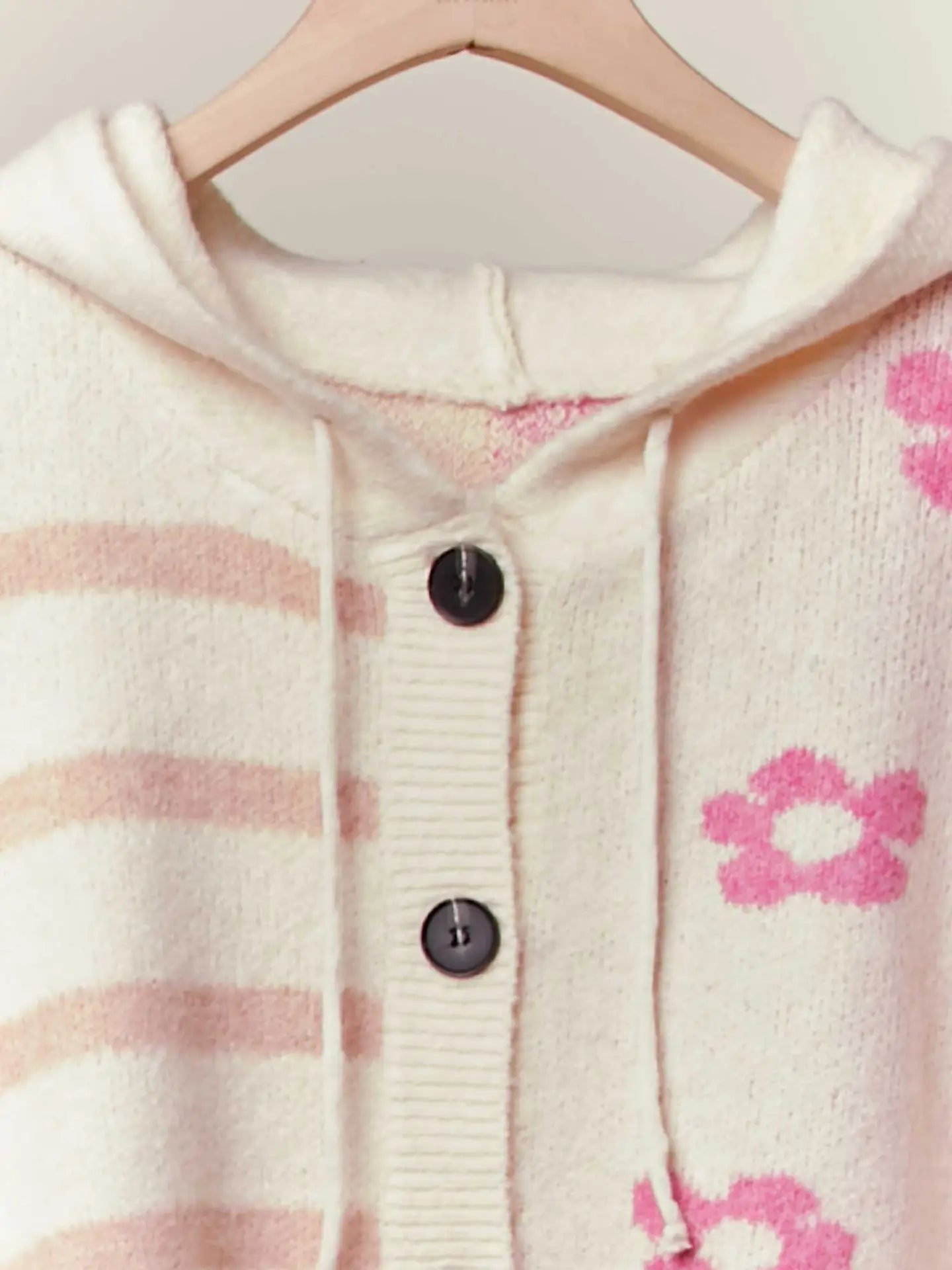 Close-up of a baby's cardigan with pink paw prints and stripes on a hanger.