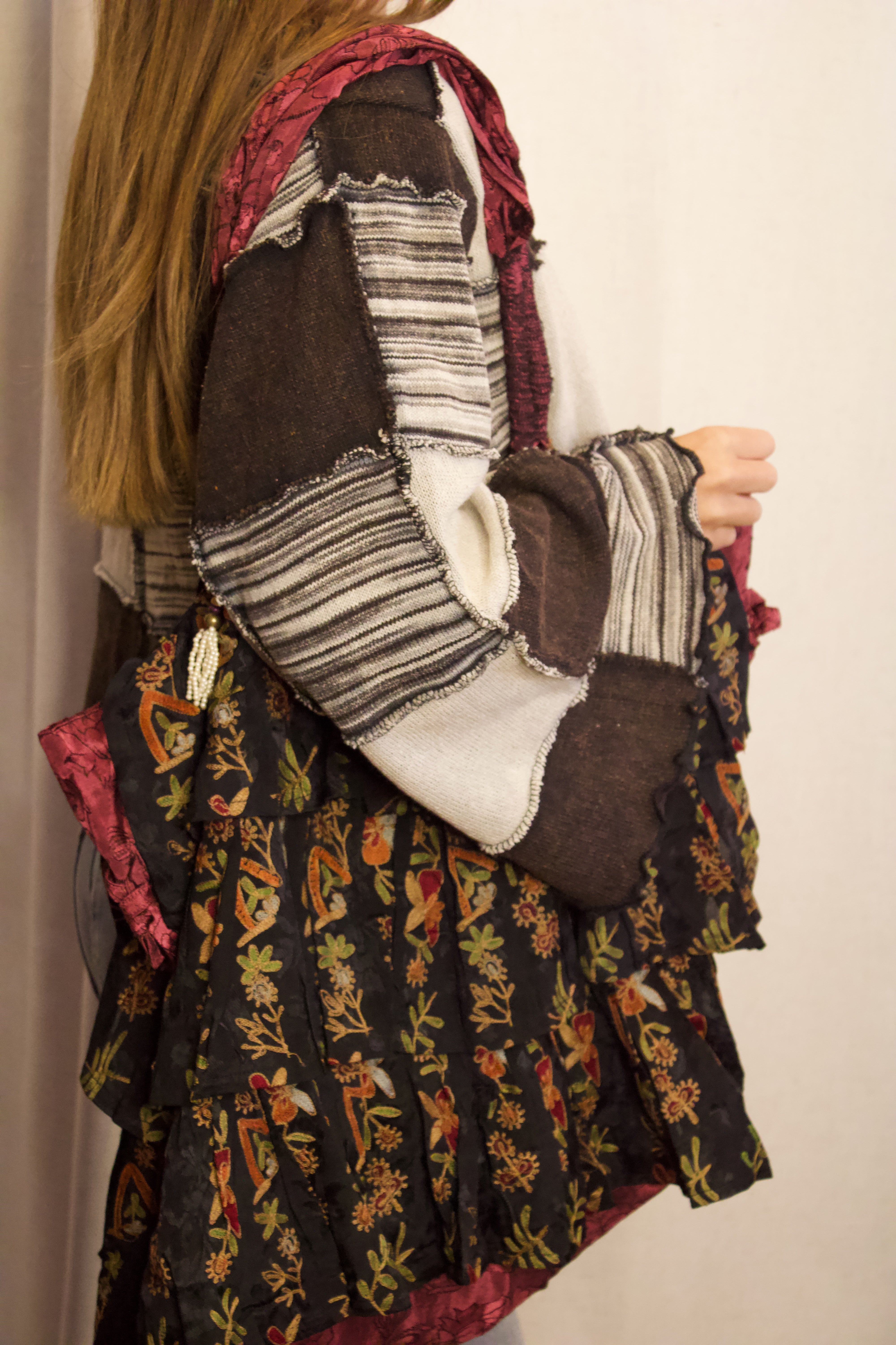 A person shown from the back wearing a patchwork-style bohemian dress with layered ruffles, featuring dark brown, black, cream, and red floral patterns.