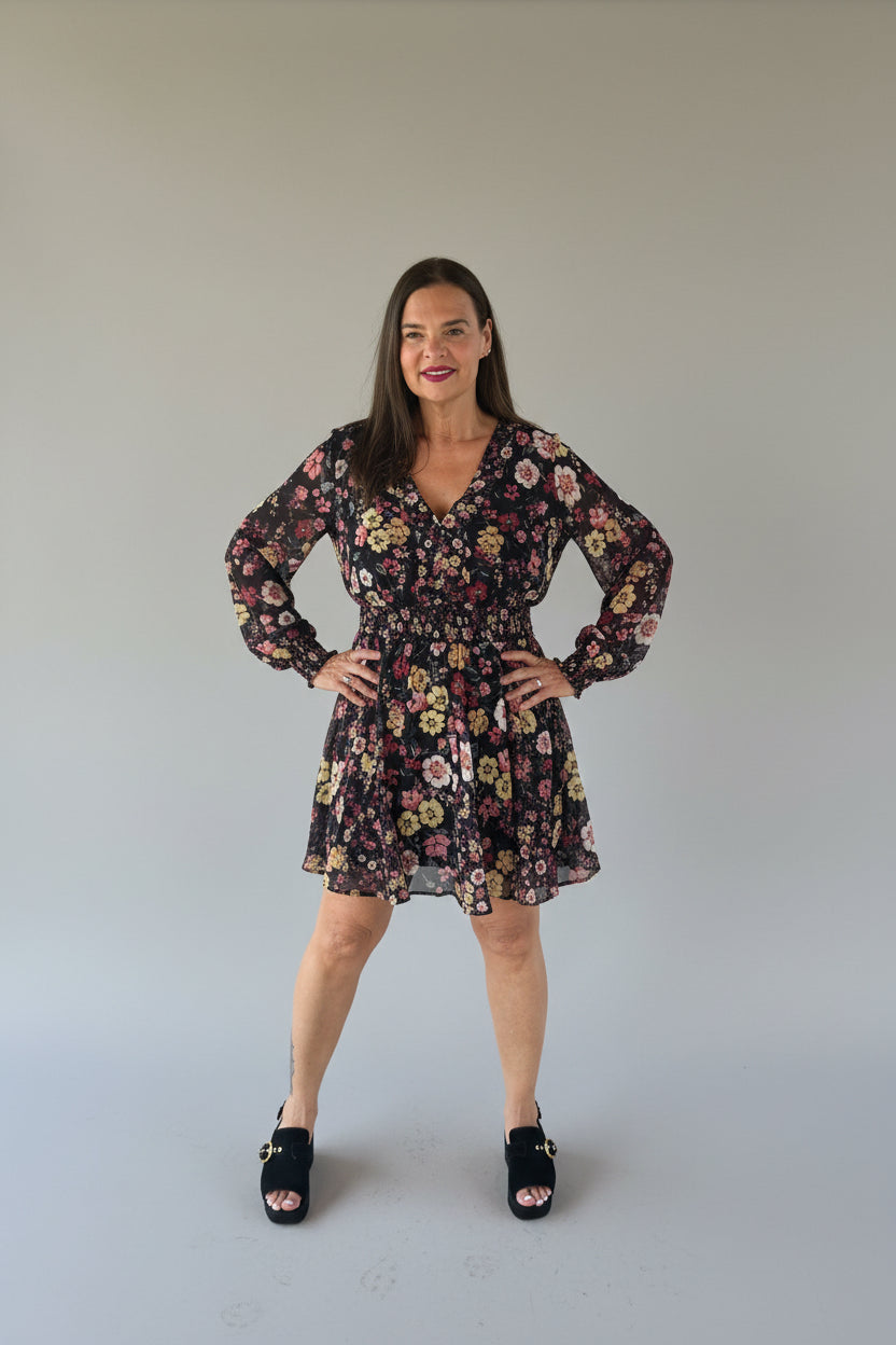 A woman modeling a black long-sleeve floral mini dress with a ruffled hem and tie waist.