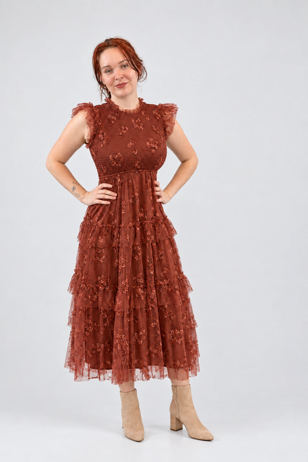 A woman modeling a rust-colored lace dress with ruffled sleeves.