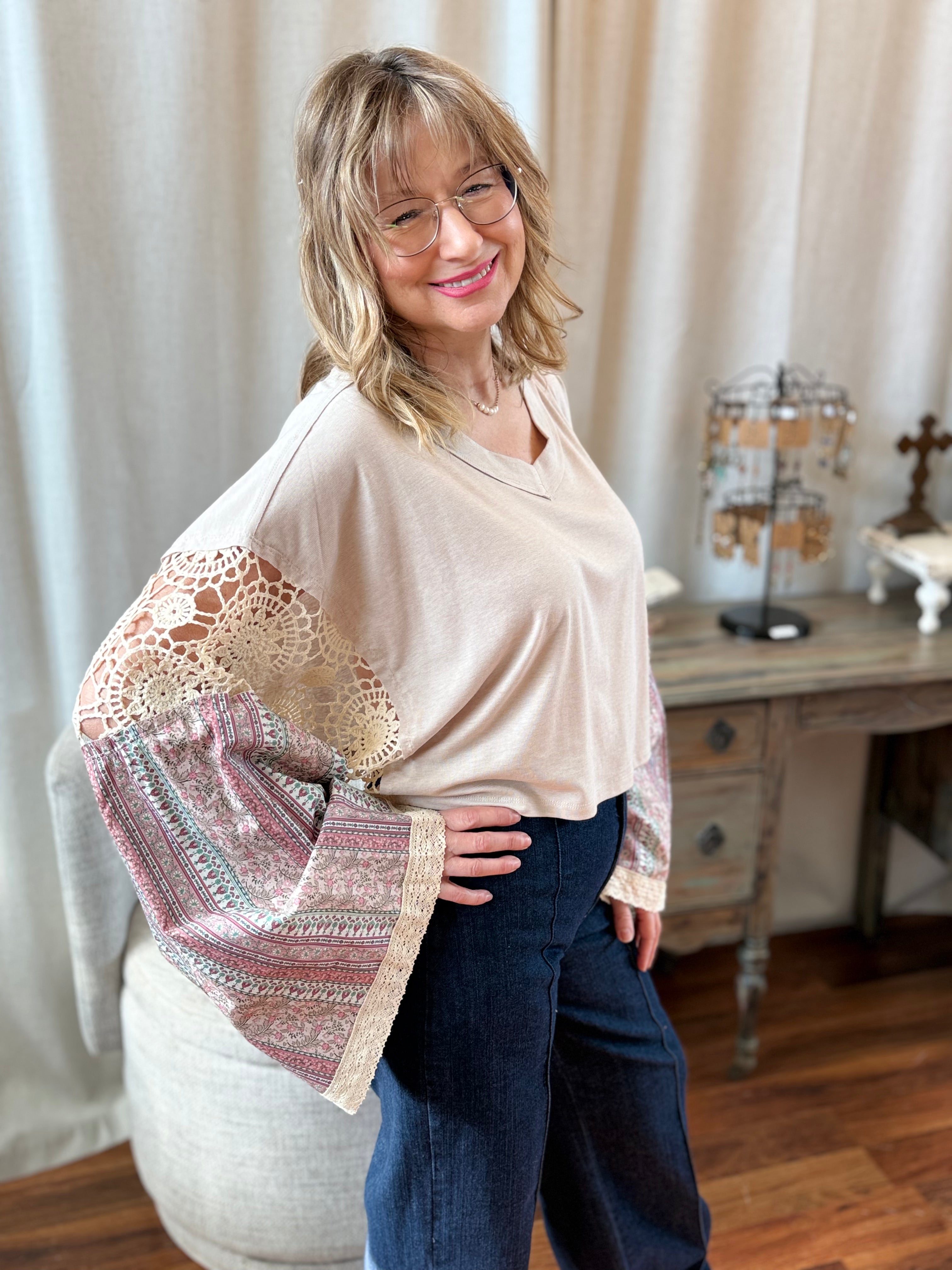 Woman wearing a beige blouse with patterned sleeves in a room with a wooden desk and decorative items.