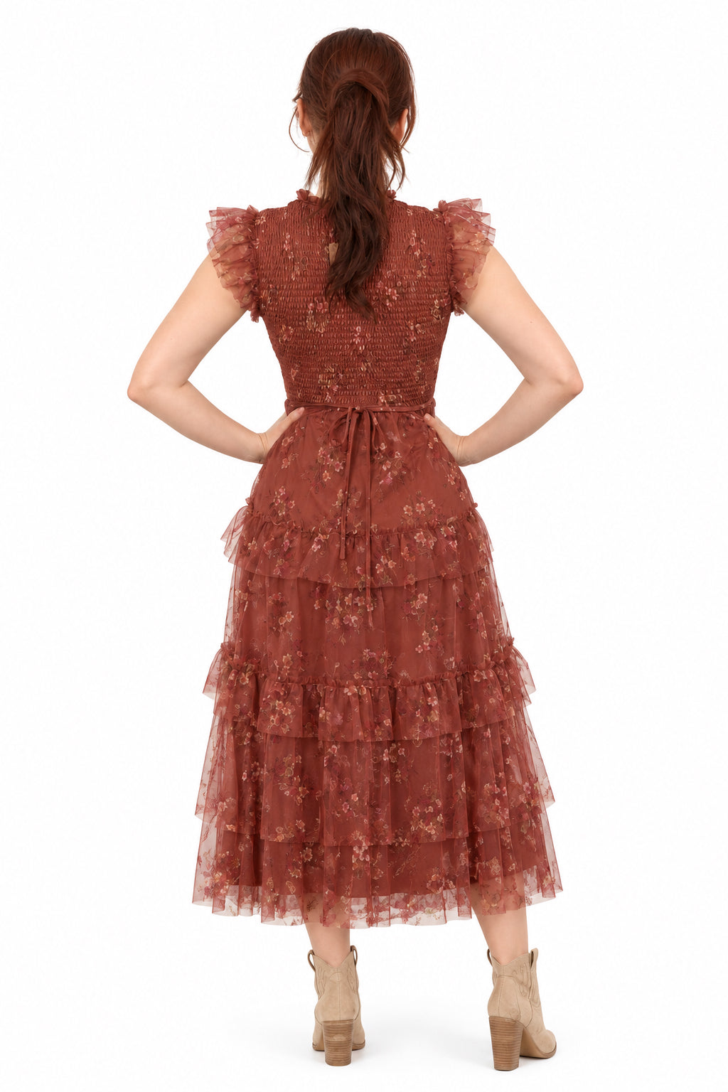 A woman stands with her back to the camera wearing a dusty rose terracotta tiered tulle dress with ruffled sleeves.
