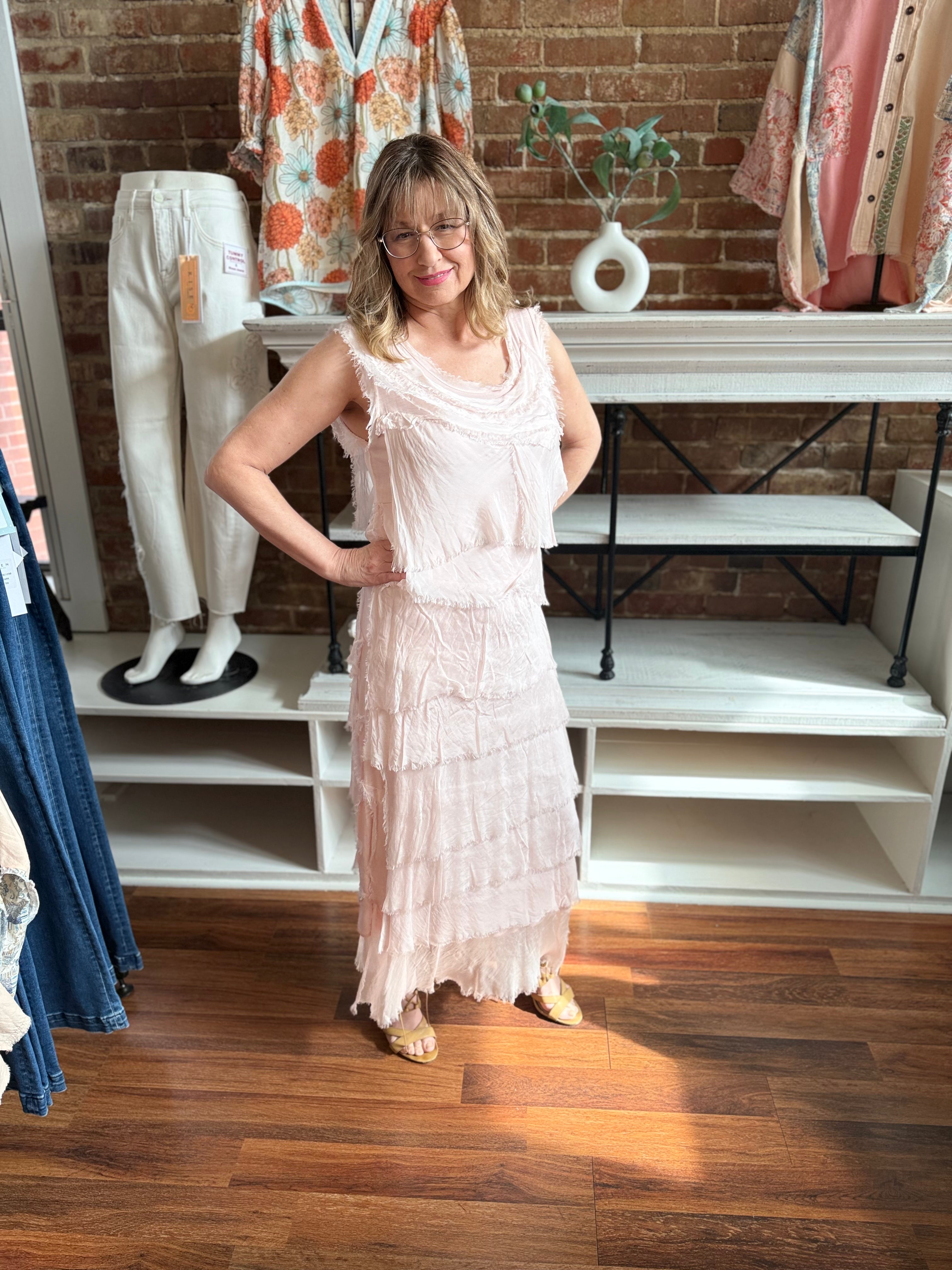 Woman in a light pink dress standing in a clothing store with mannequins and clothing in the background.