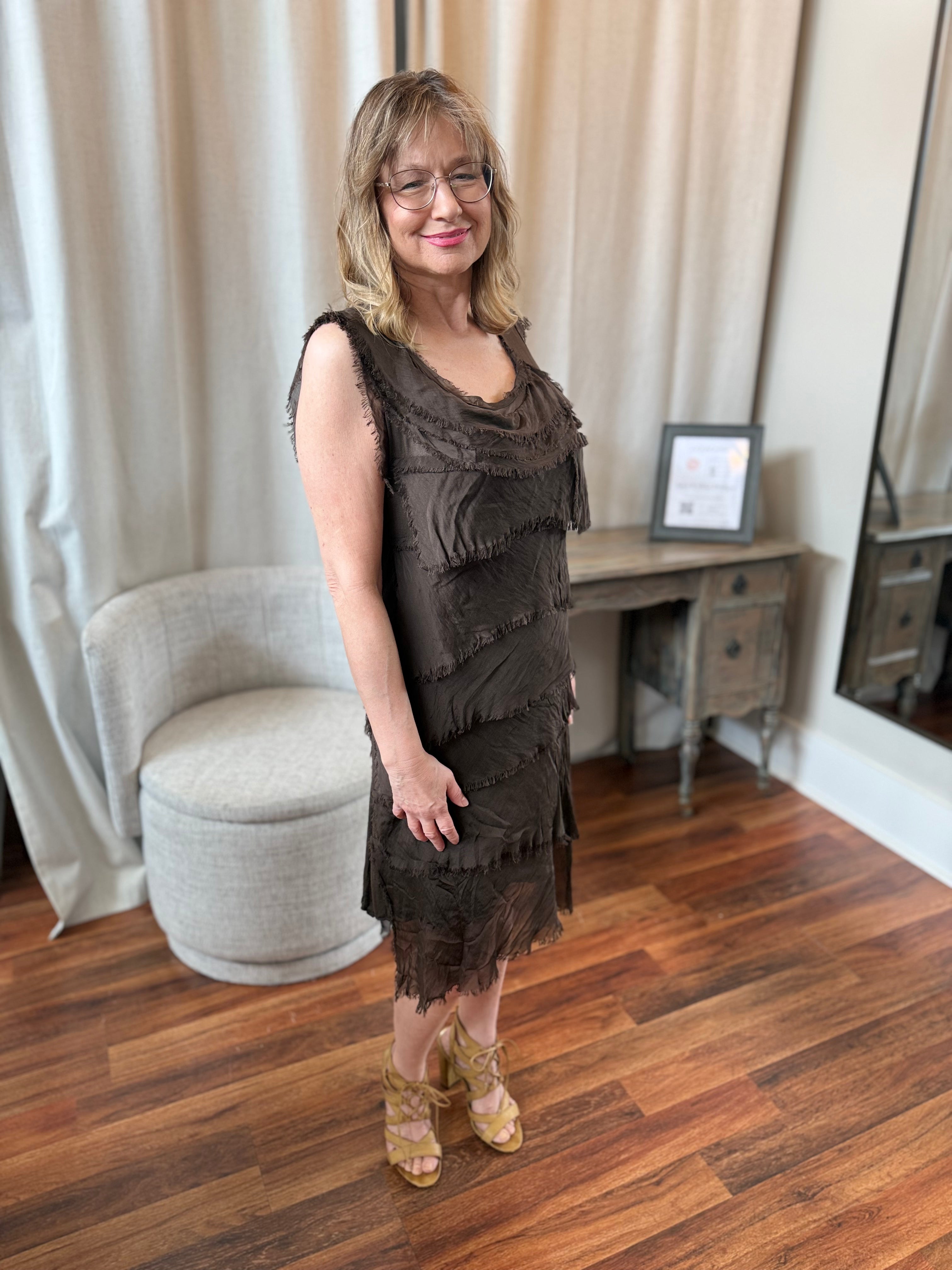 Woman in a brown lace dress standing in a room with wooden flooring and neutral decor.