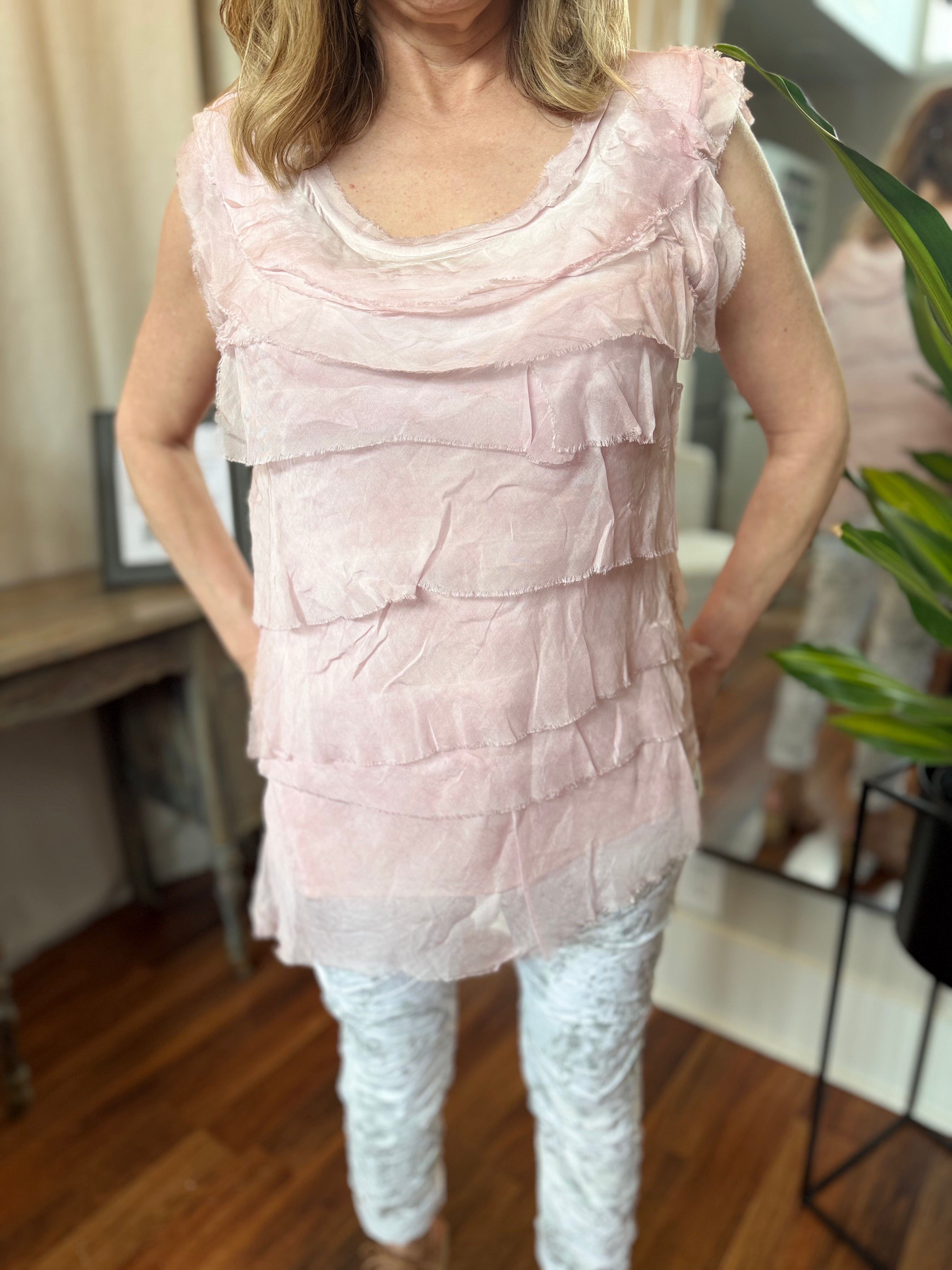 Woman wearing a light pink ruffled top and white pants in an indoor setting.