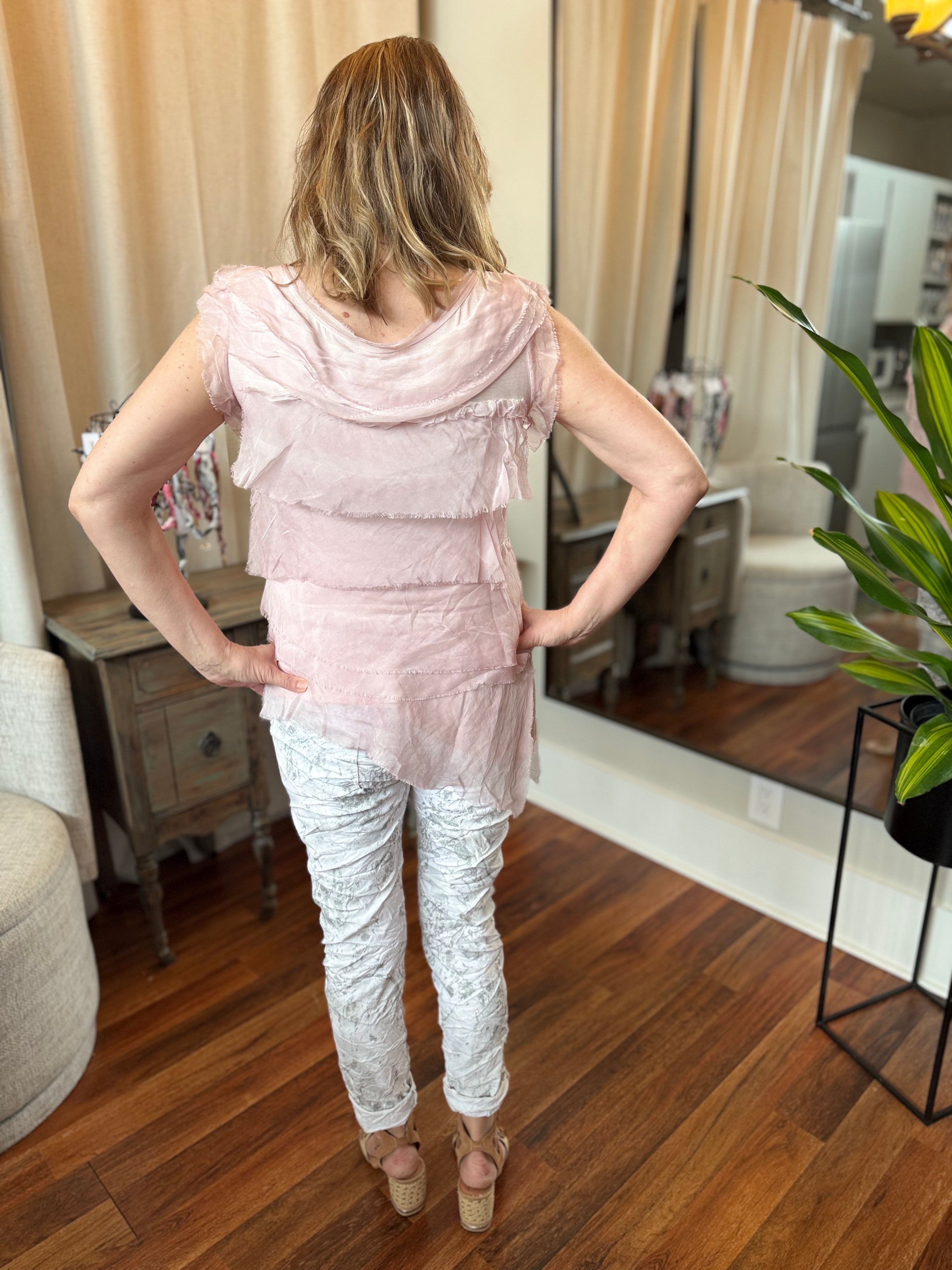 Woman wearing a pink top and white lace pants in a room with wooden floor and mirror.