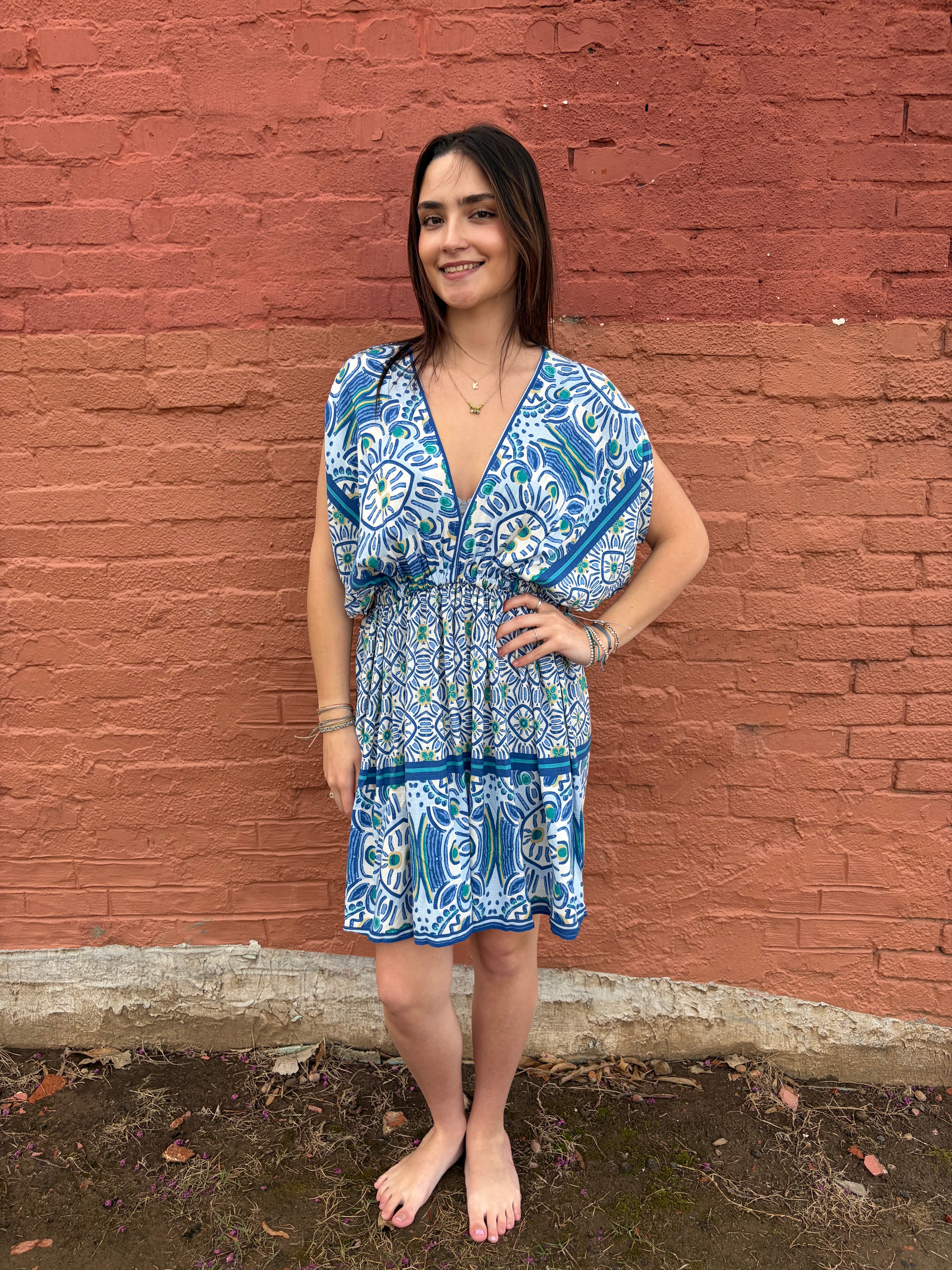 Woman in a blue patterned dress standing on a red brick surface.