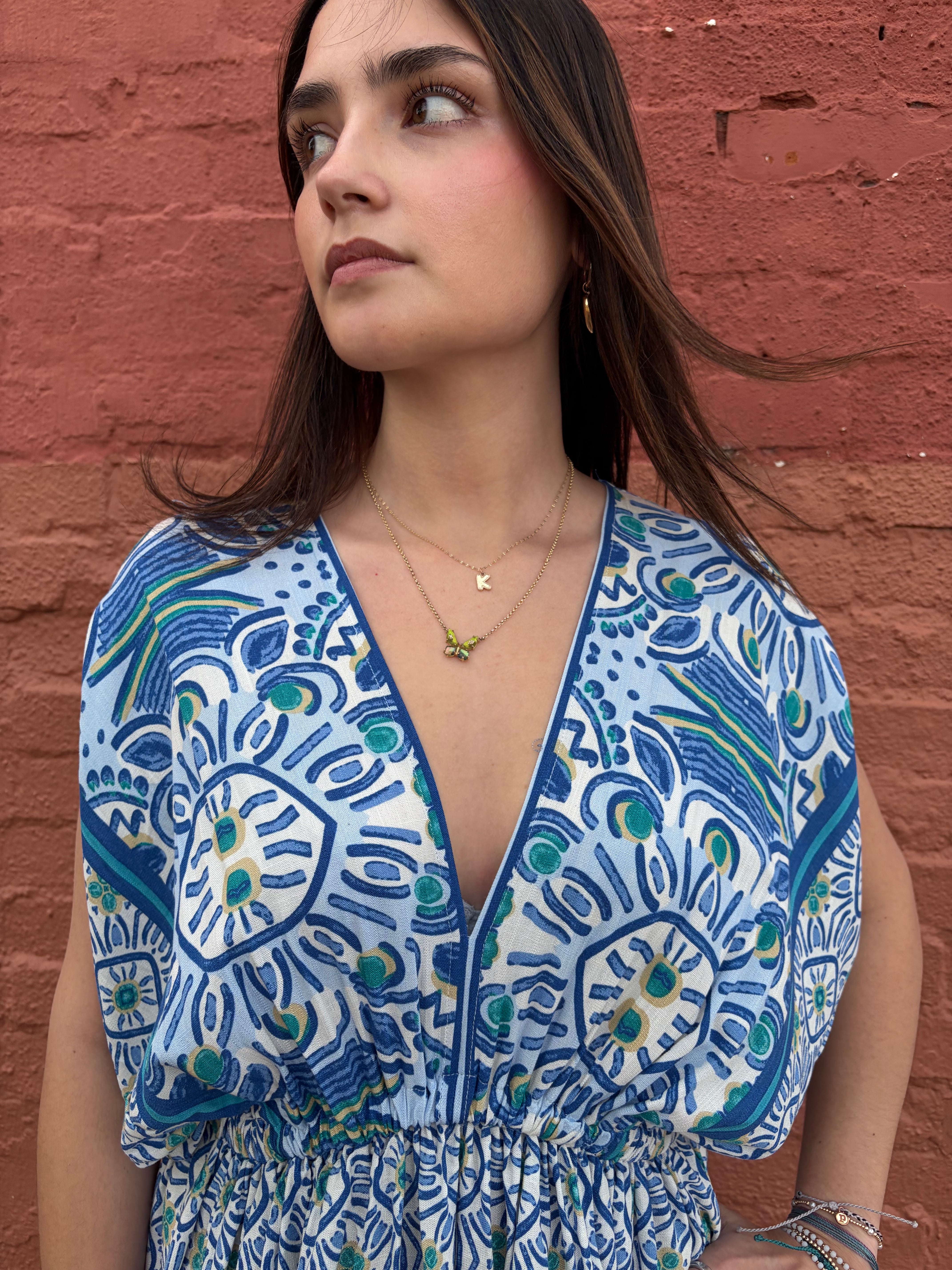 Woman wearing a blue and white patterned dress against a red brick wall.