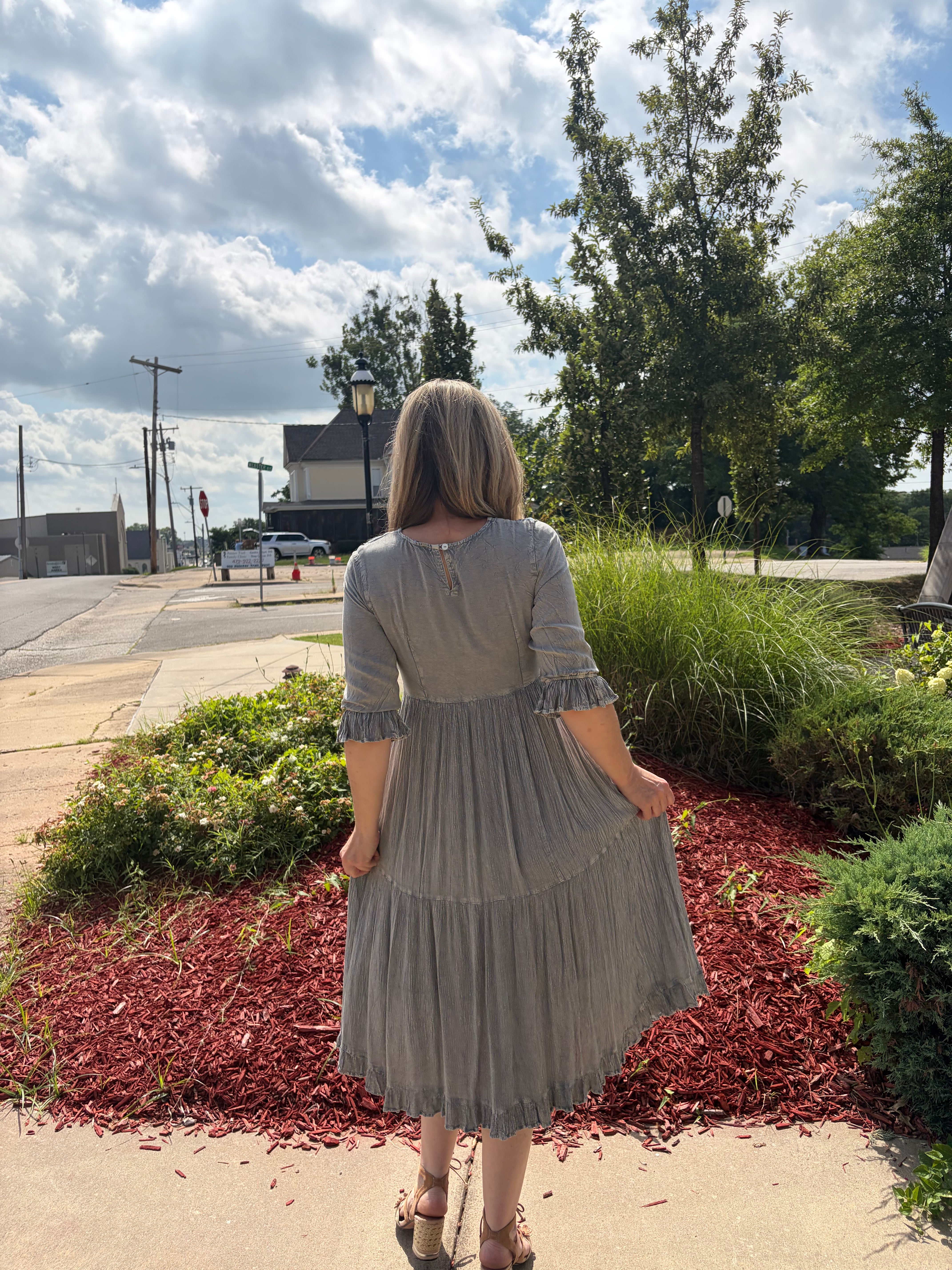ack view of grey denim fusion tiered midi dress showing 3/4 bell sleeves, tiered skirt, and fringe hem detail 