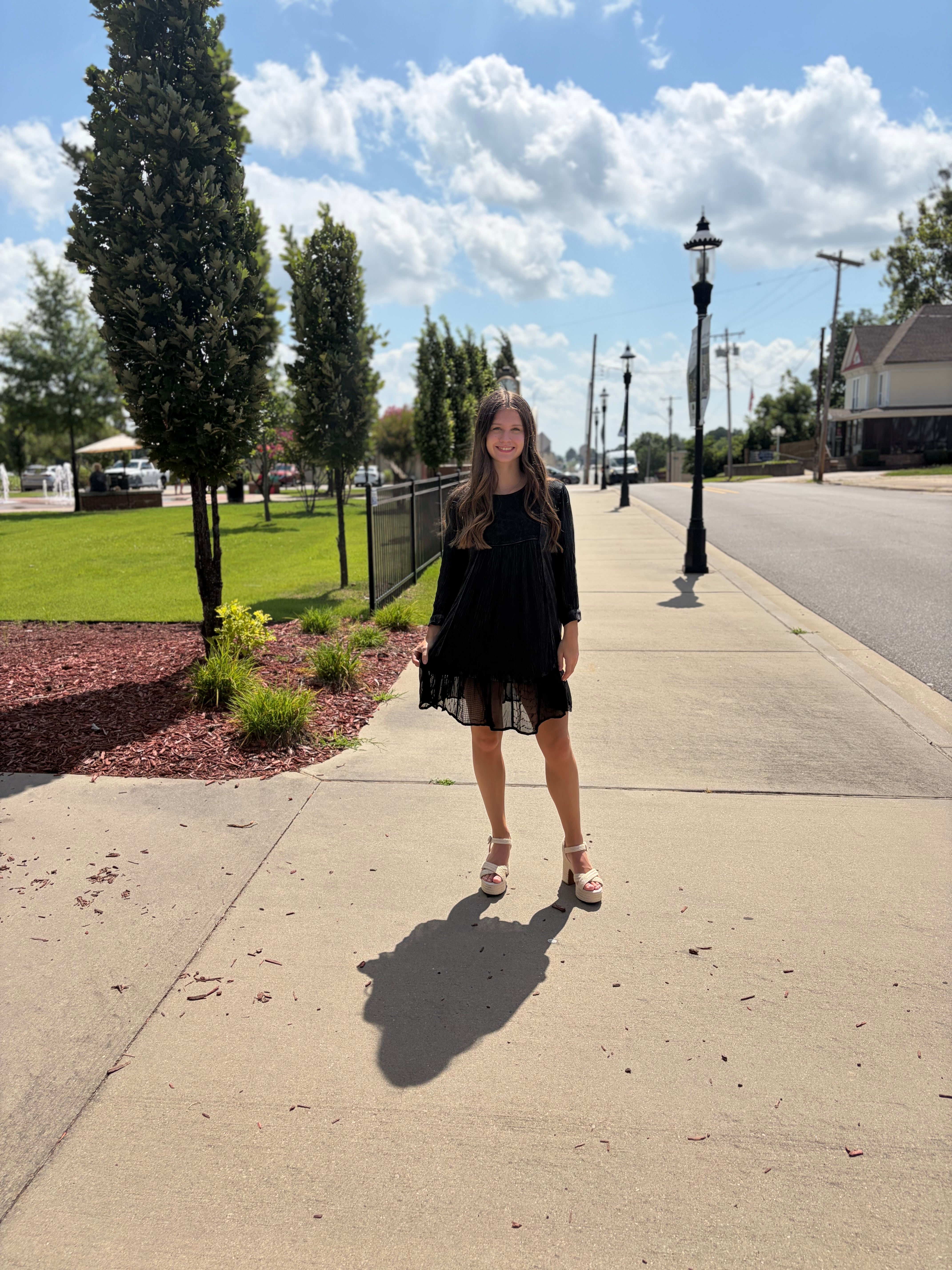 Black embroidered babydoll dress with 3/4 sleeves and ruffle hem styled on a sunny sidewalk