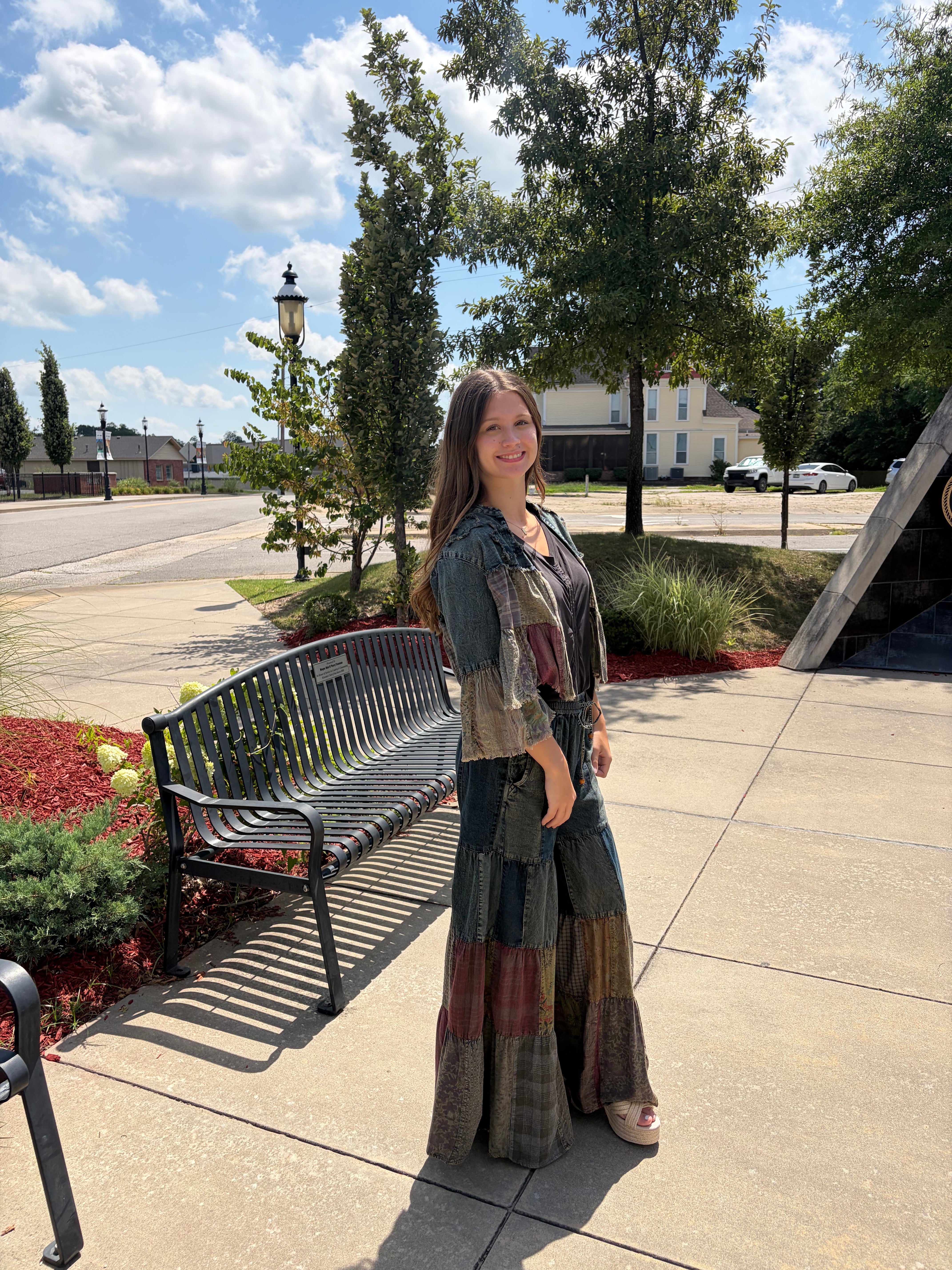 Full front lifestyle shot, model smiling, shrug styled open over a patchwork maxi skirt, outdoor setting