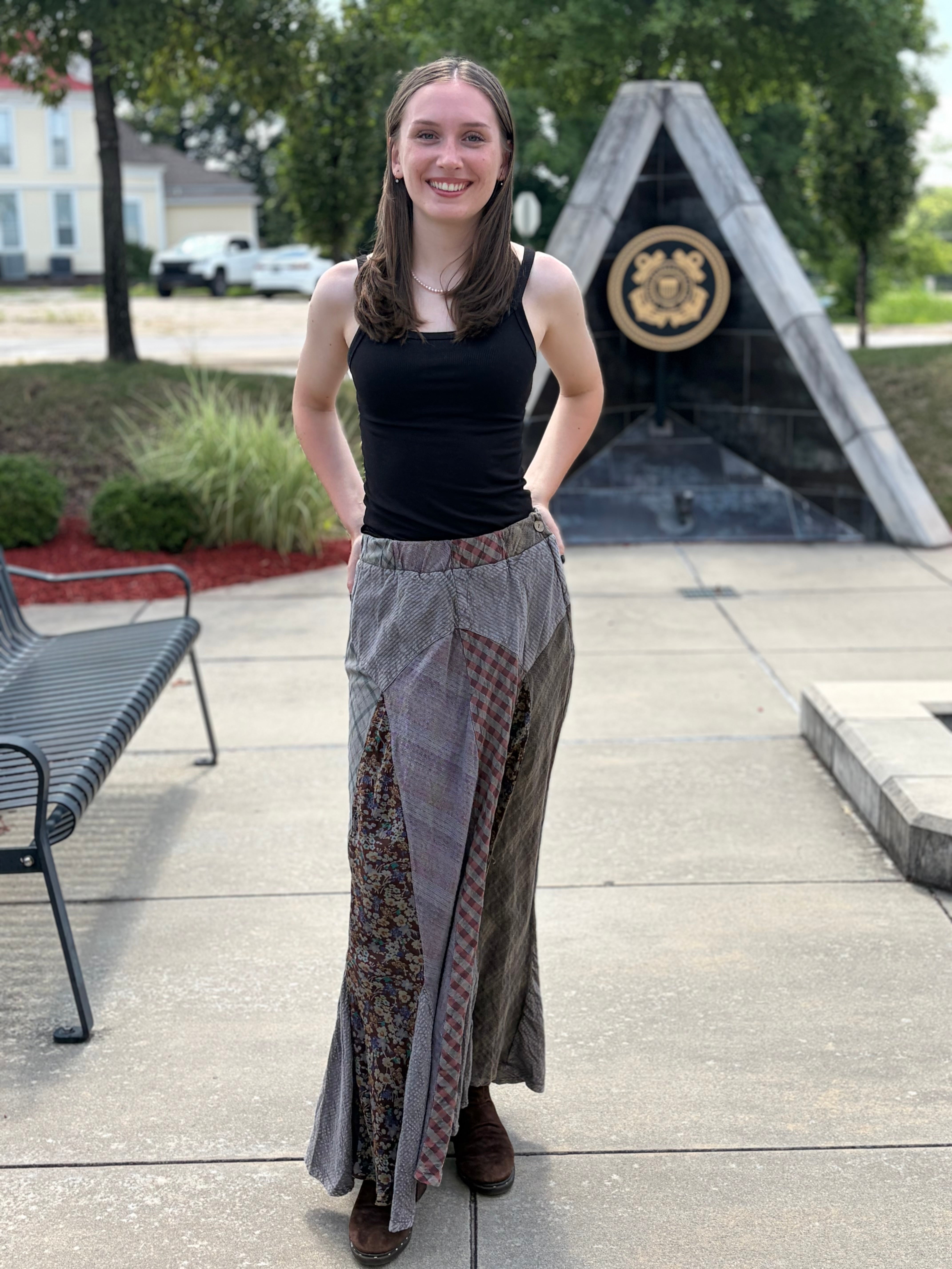 Woman smiling in Montana patchwork maxi skirt with mixed plaid floral and houndstooth panels, styled with black tank top and brown boots, full front view