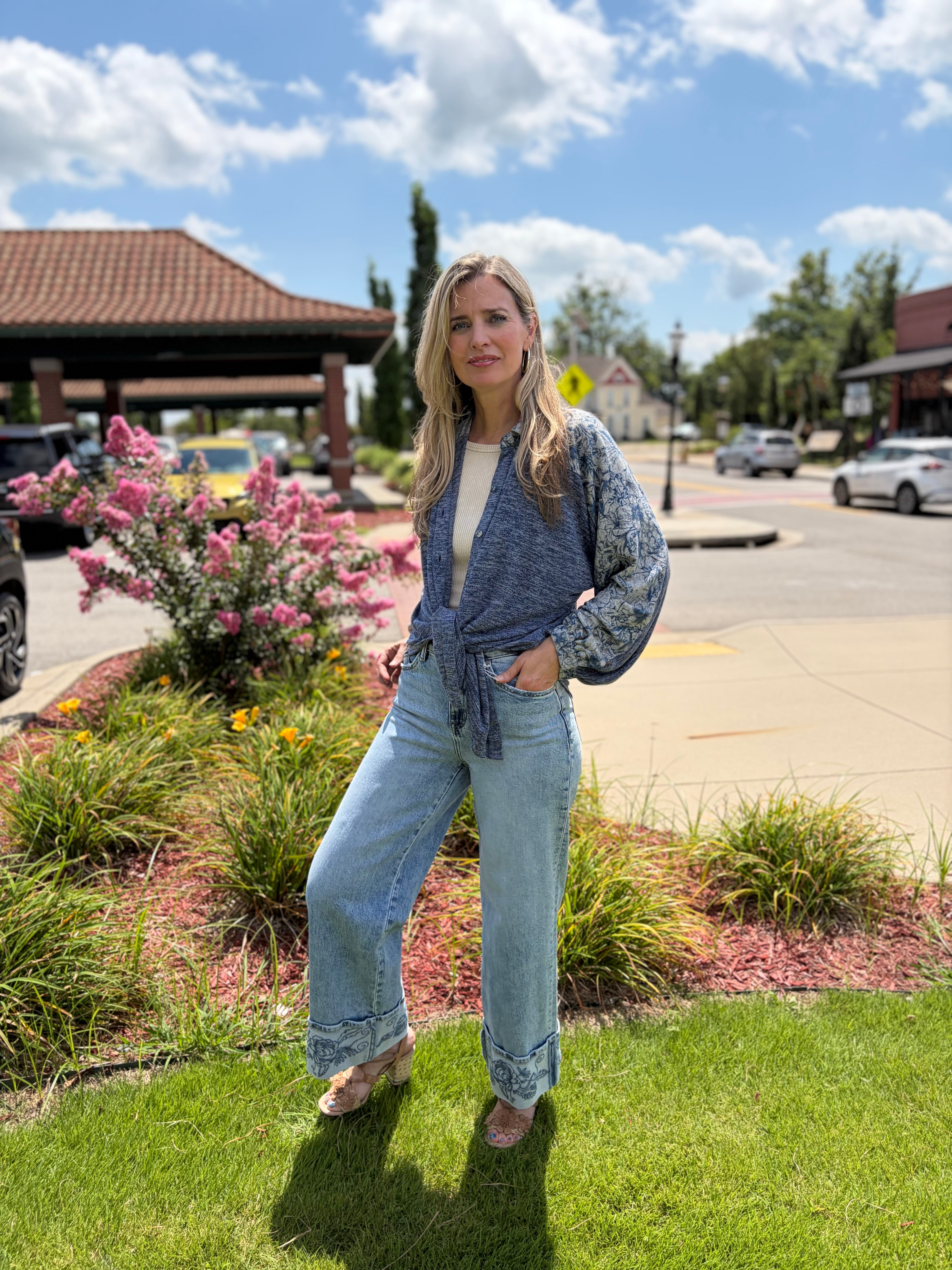 Front lifestyle shot of woman in bohemian blue sweater knit shirt with floral print sleeves and front tie, paired with wide-leg light wash jeans
