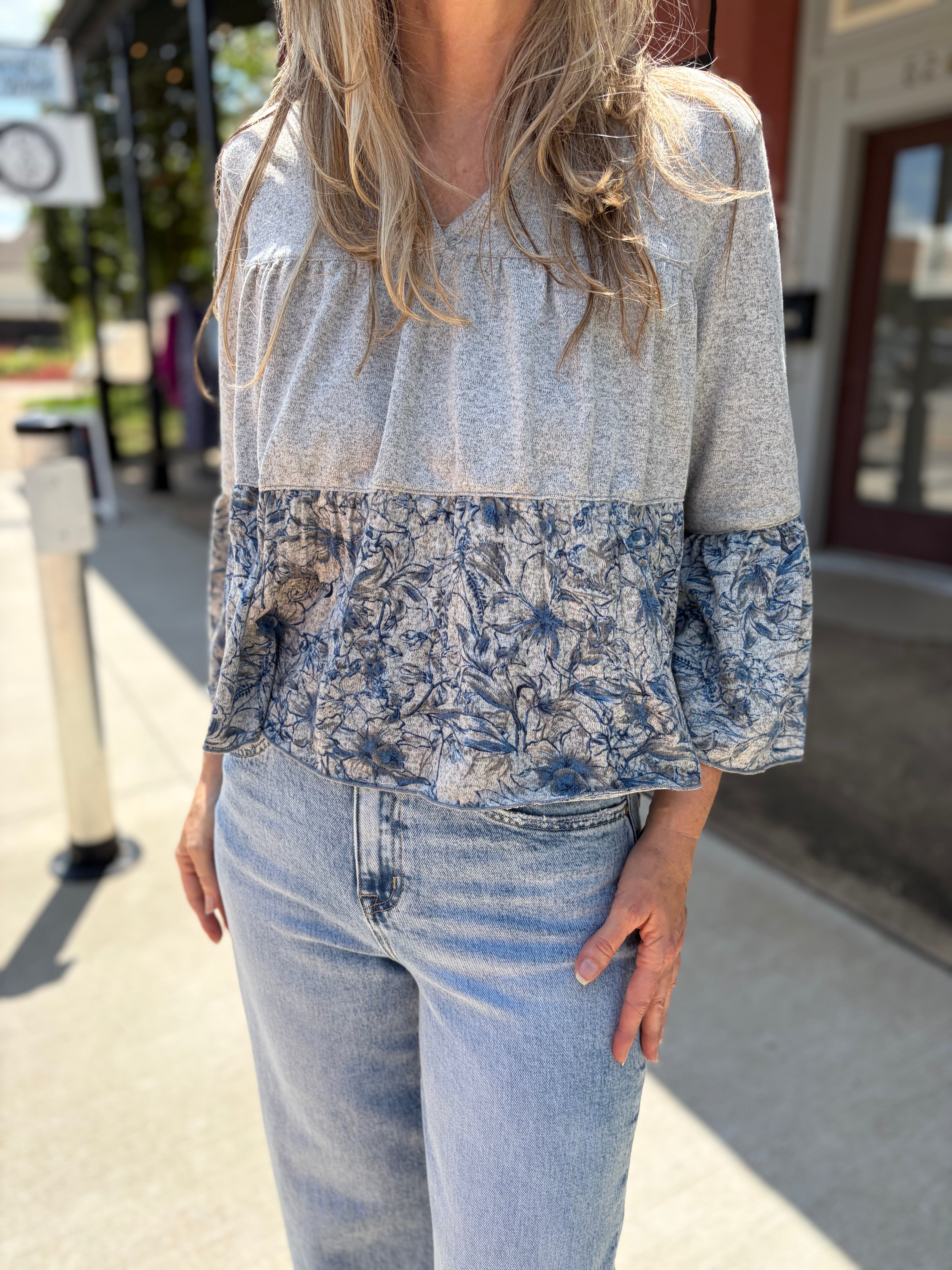Close-up front detail, heathered gray upper + bold blue floral smocked lower panel + ruffled cuffs