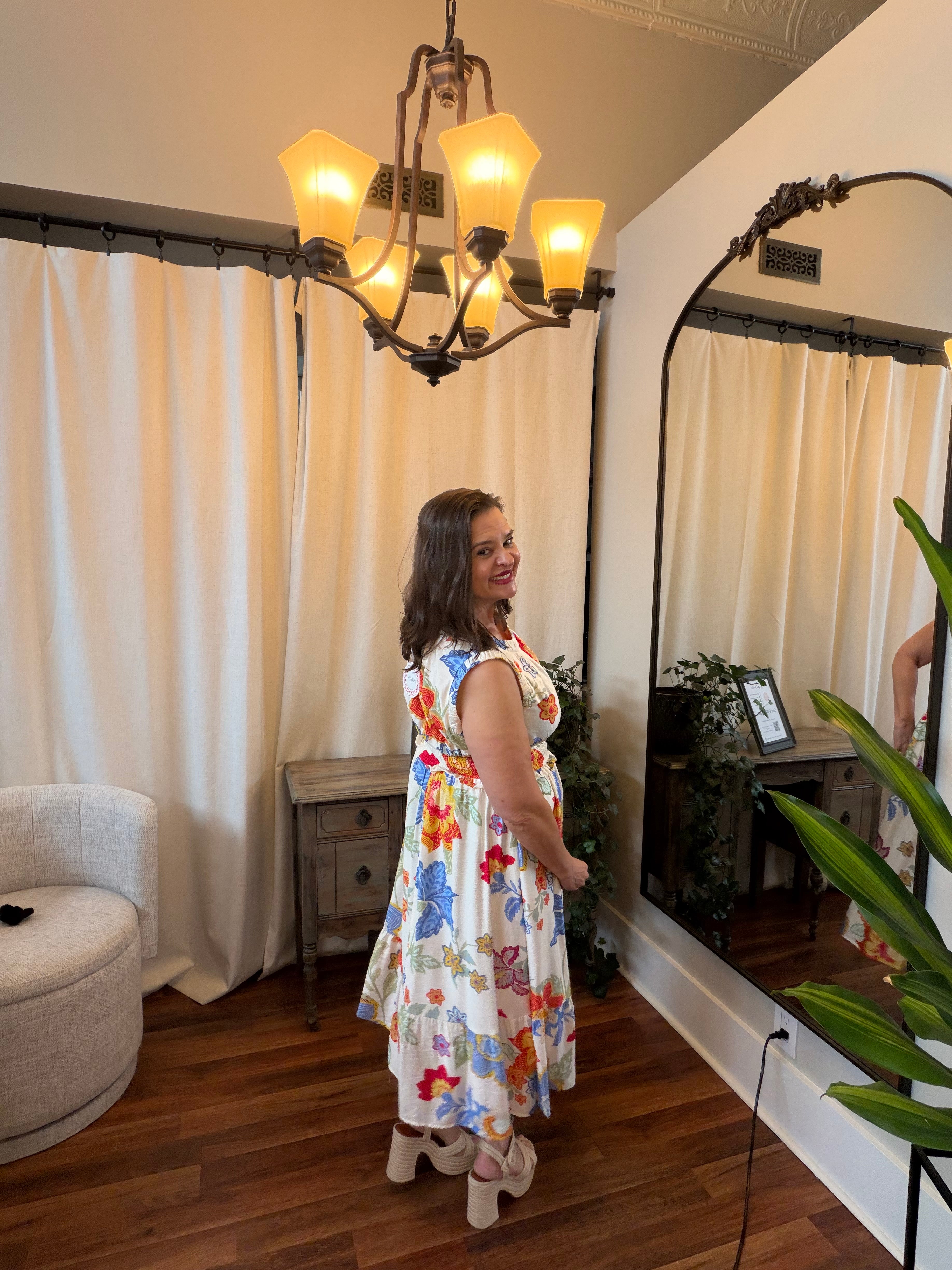 Woman in a floral dress standing in a room with a chandelier and large mirror.