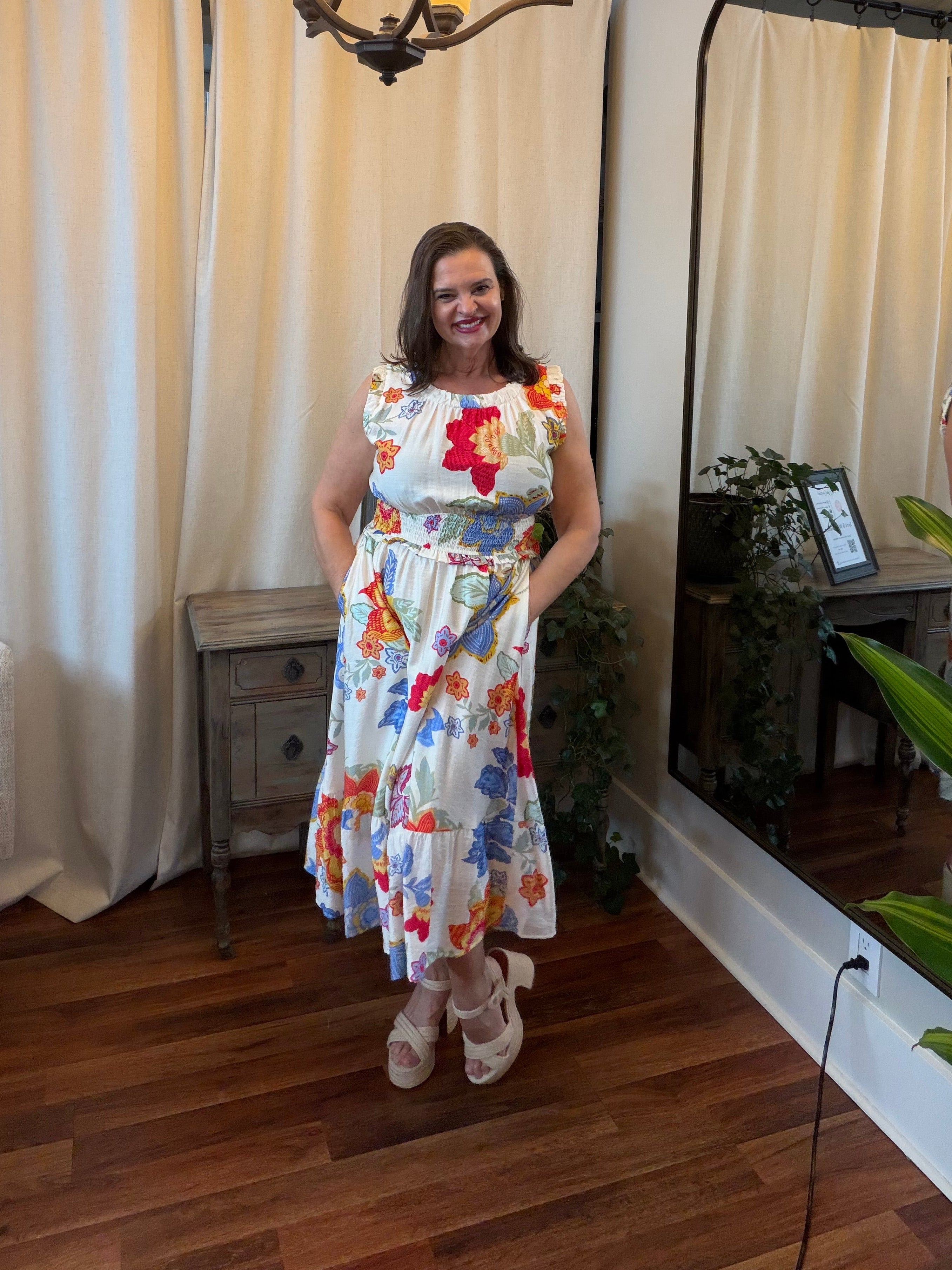 Woman in a floral dress standing in a room with a chandelier and large mirror.