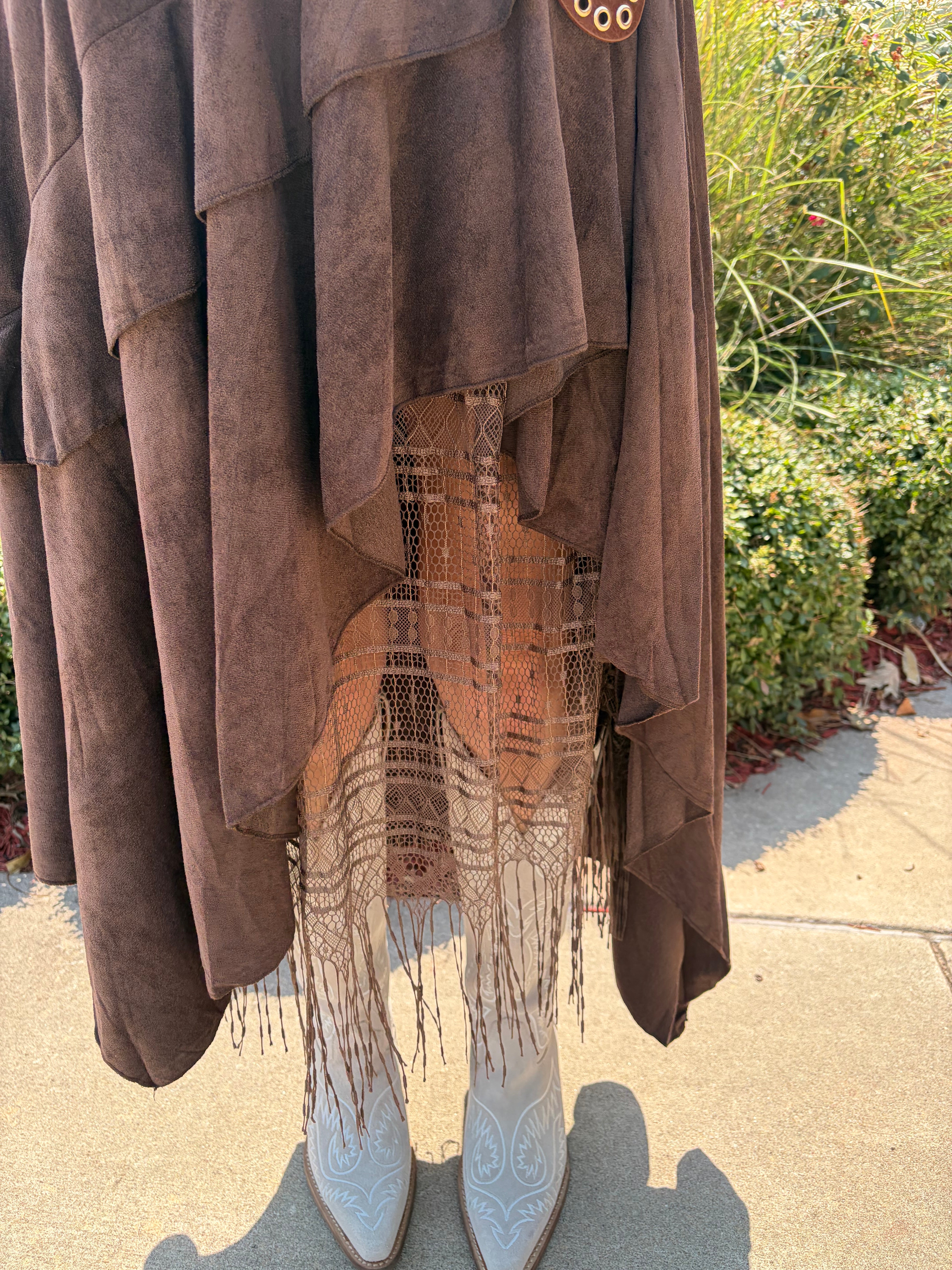 Close-up detail of Boho Layered Lace Skirt showing dark brown suede-like asymmetrical tiers, sheer lace underlayer, and long fringe hem with white cowboy boots