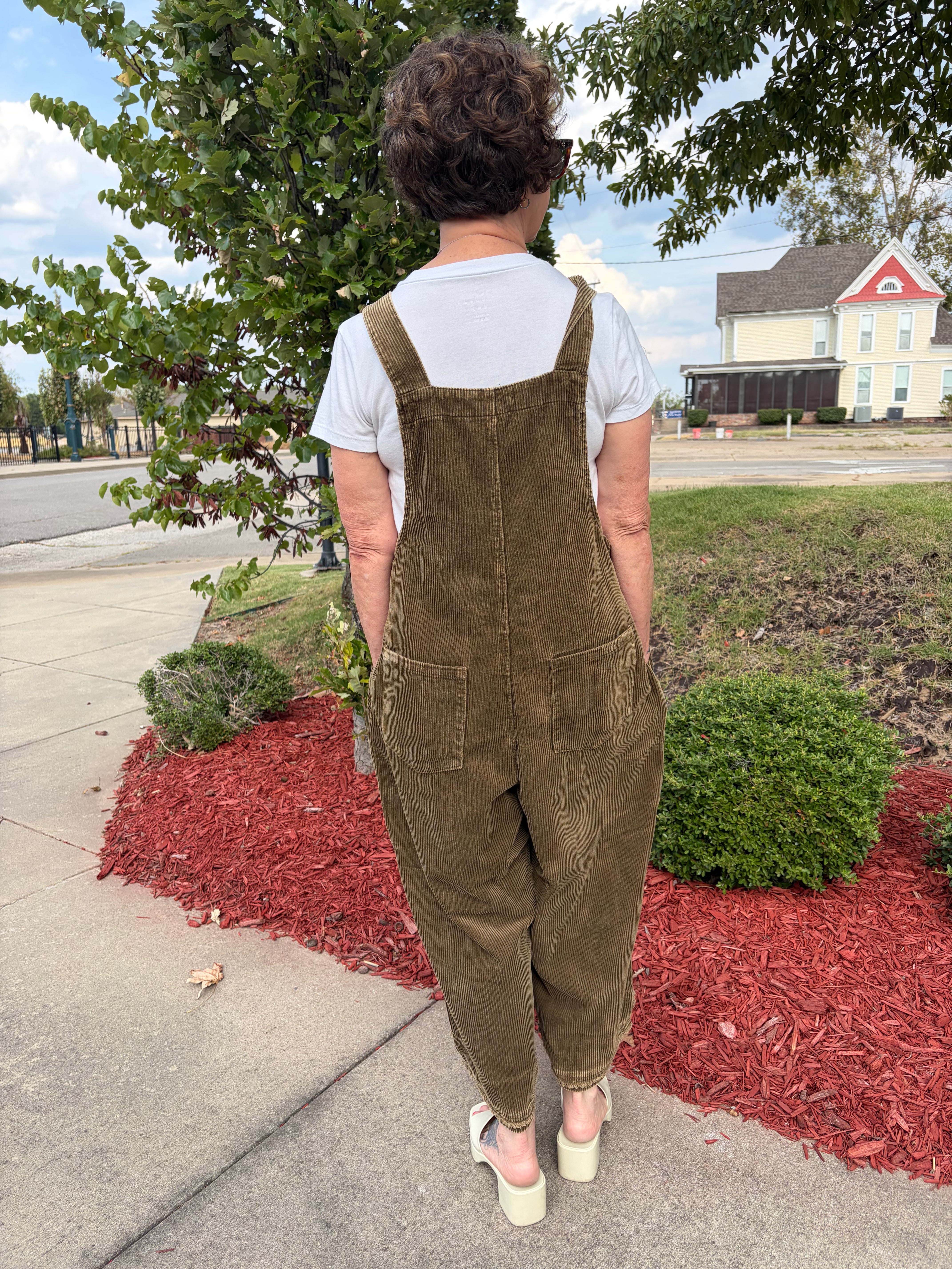 Back view of woman wearing olive green Flower Patch Corduroy Wide-Leg Overalls showing adjustable straps, large back pocket, and relaxed wide-leg silhouette
