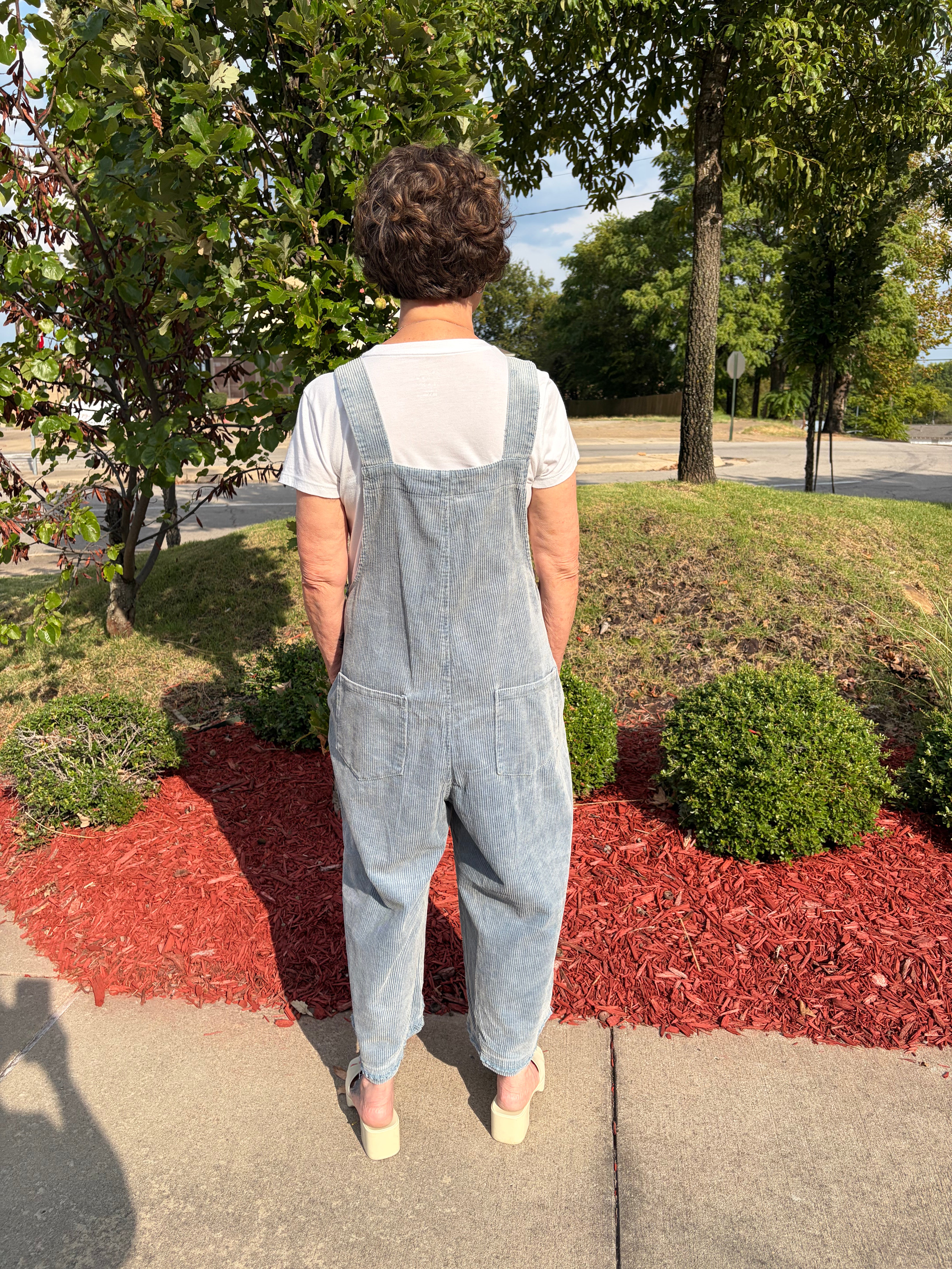 Back view of woman wearing olive green Flower Patch Corduroy Wide-Leg Overalls showing adjustable straps, large back pocket, and relaxed wide-leg silhouette