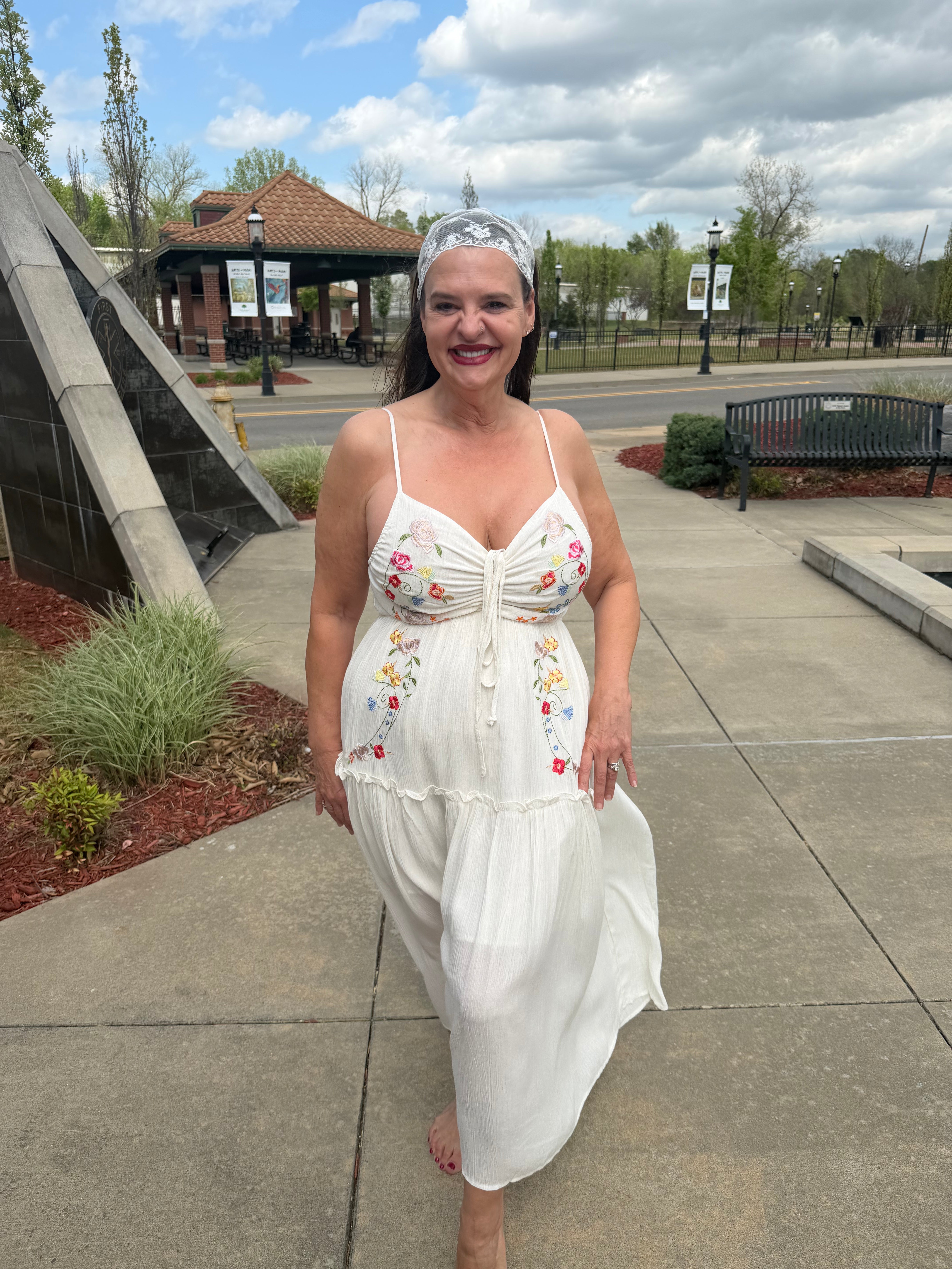Woman in a white floral dress standing on a sidewalk with a park in the background