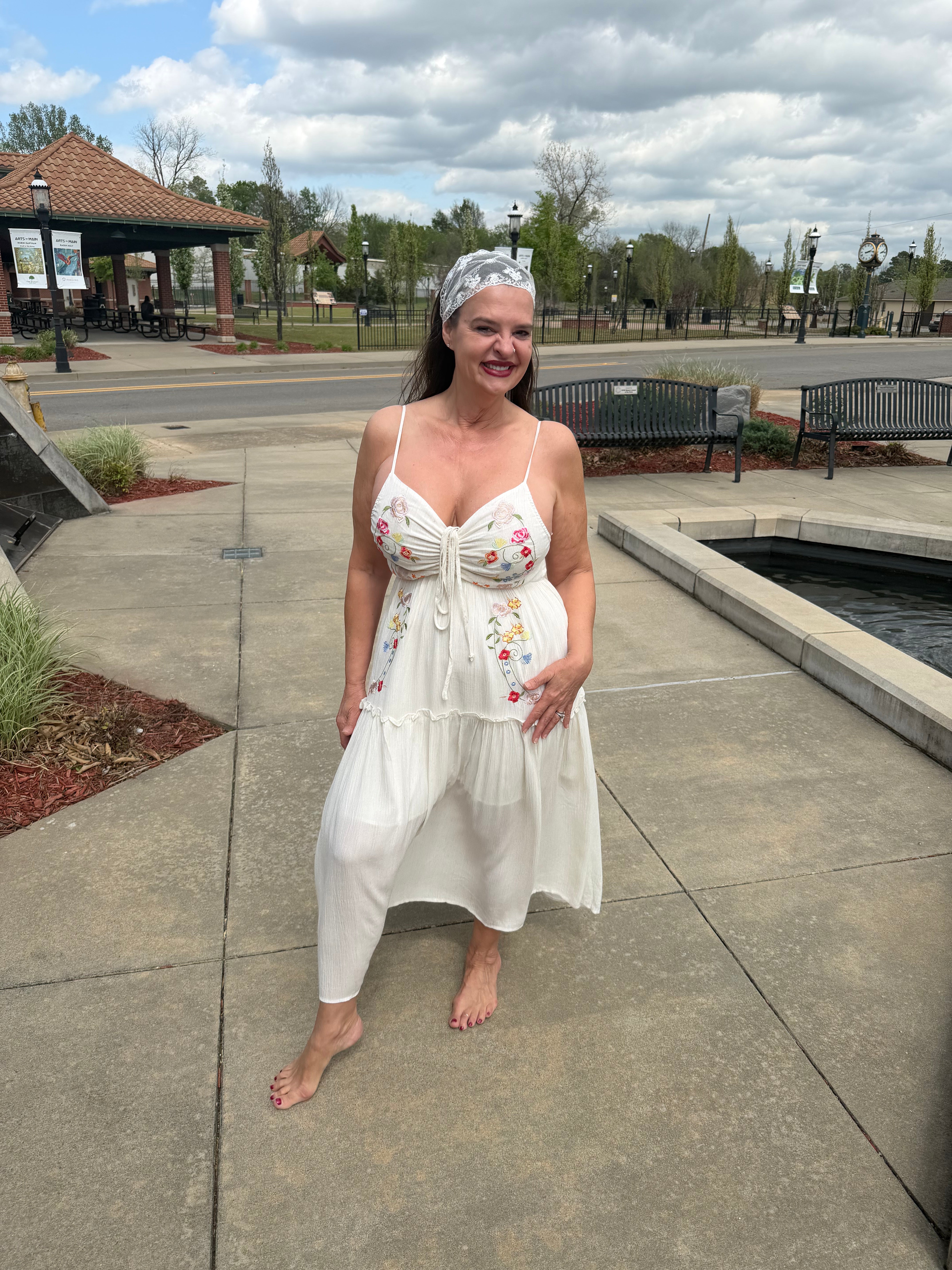 Woman in a white dress with floral patterns standing on a sidewalk.