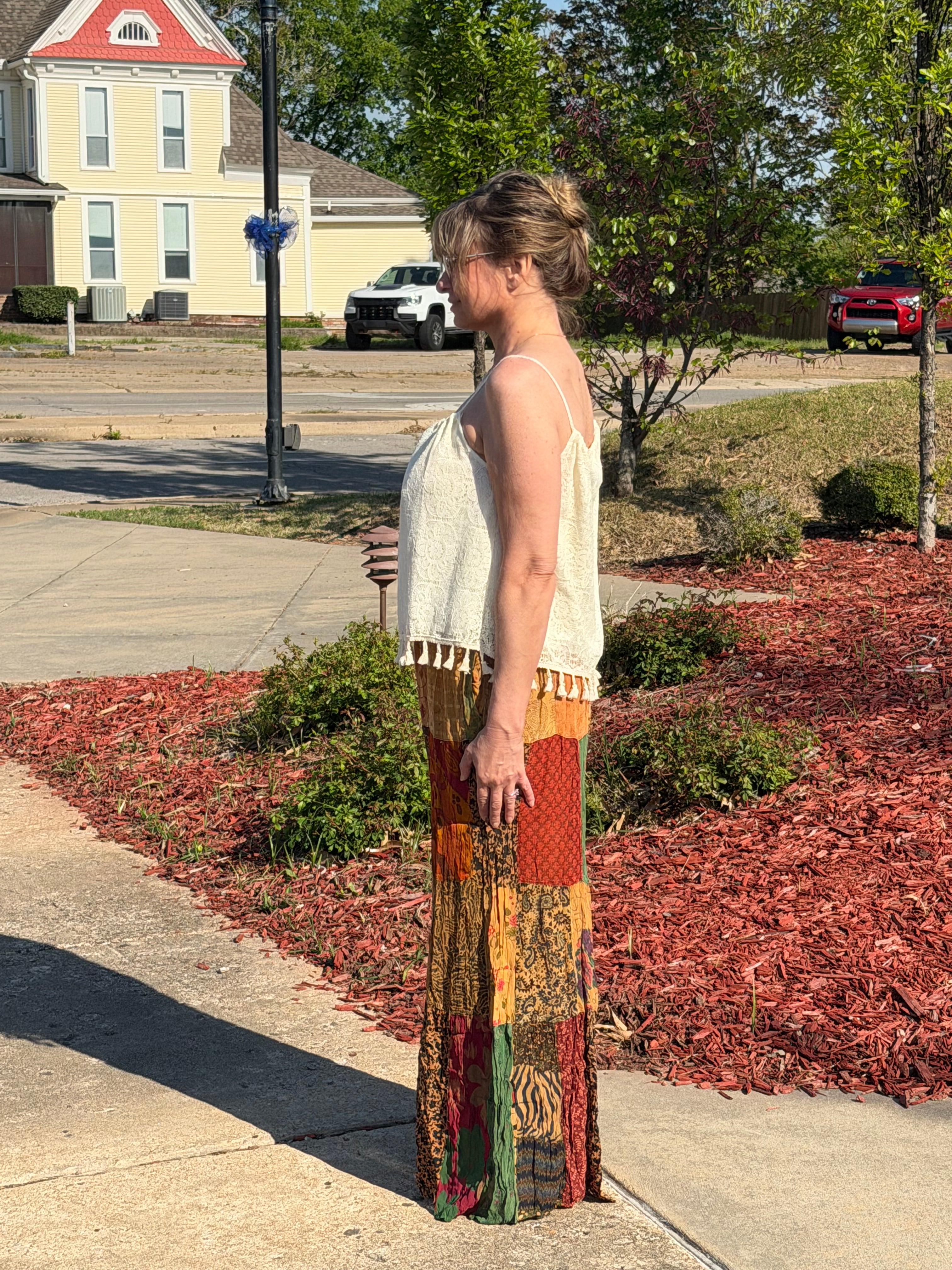 Woman wearing colorful patchwork pants and a white top in a room with decor elements.
