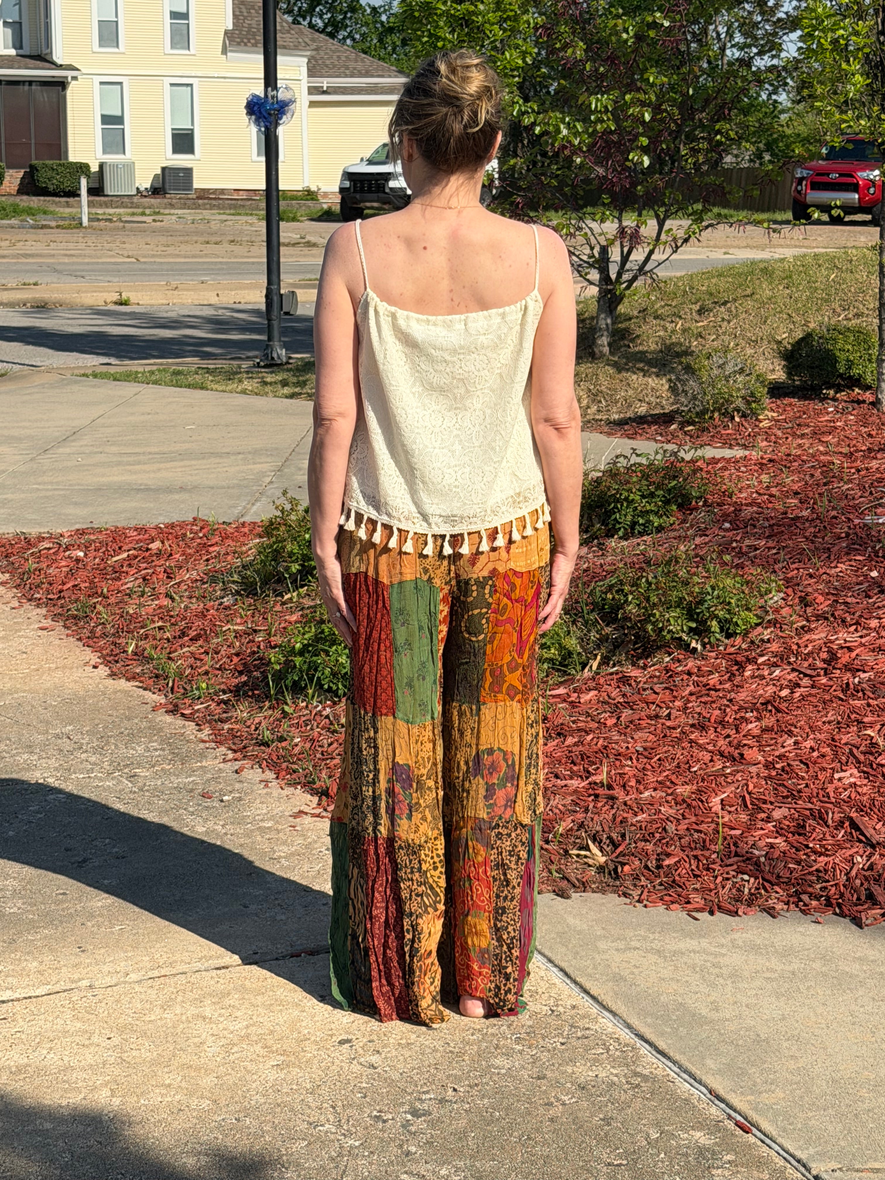 Woman wearing colorful patchwork pants and a white top in a room with decor elements.