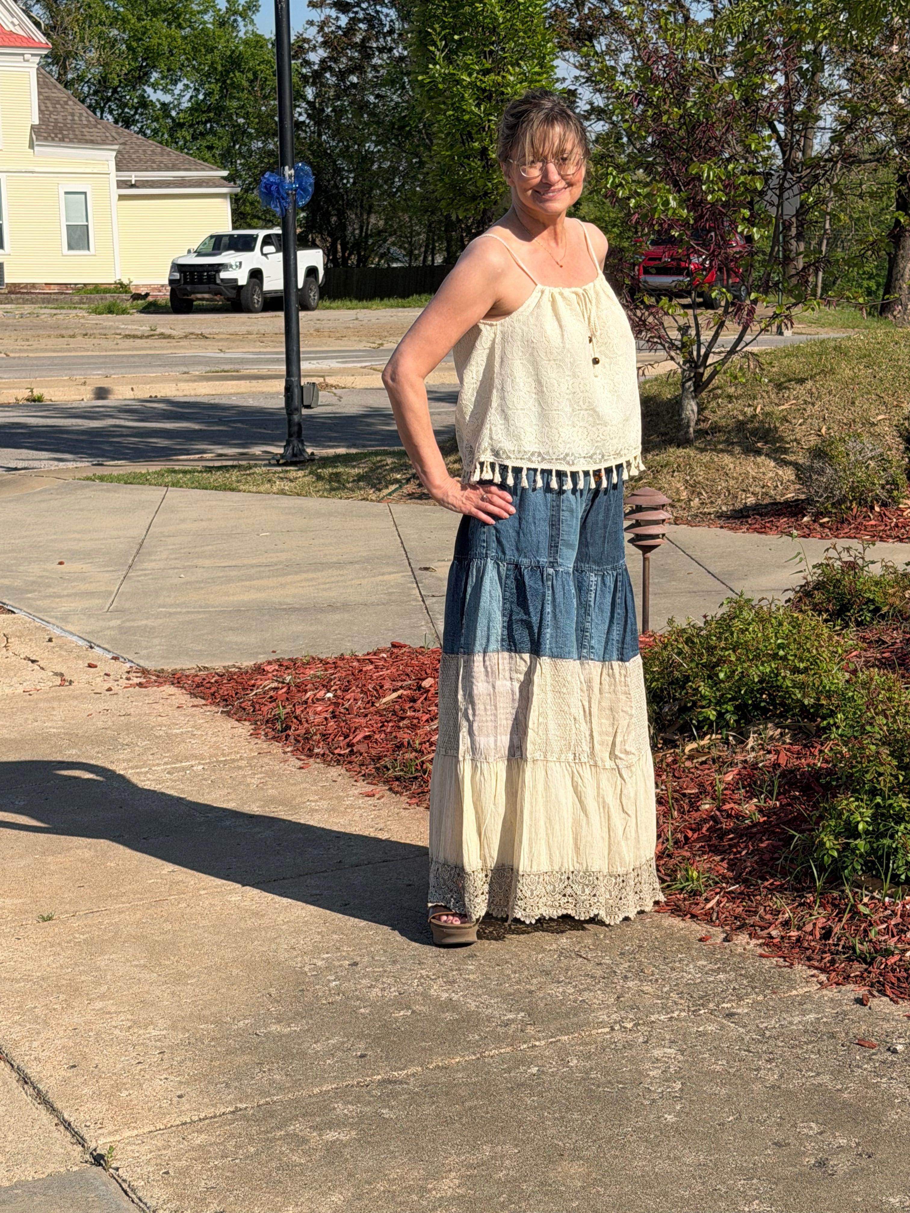 Person standing on a sidewalk with a long, light-colored dress draped over their shoulders.