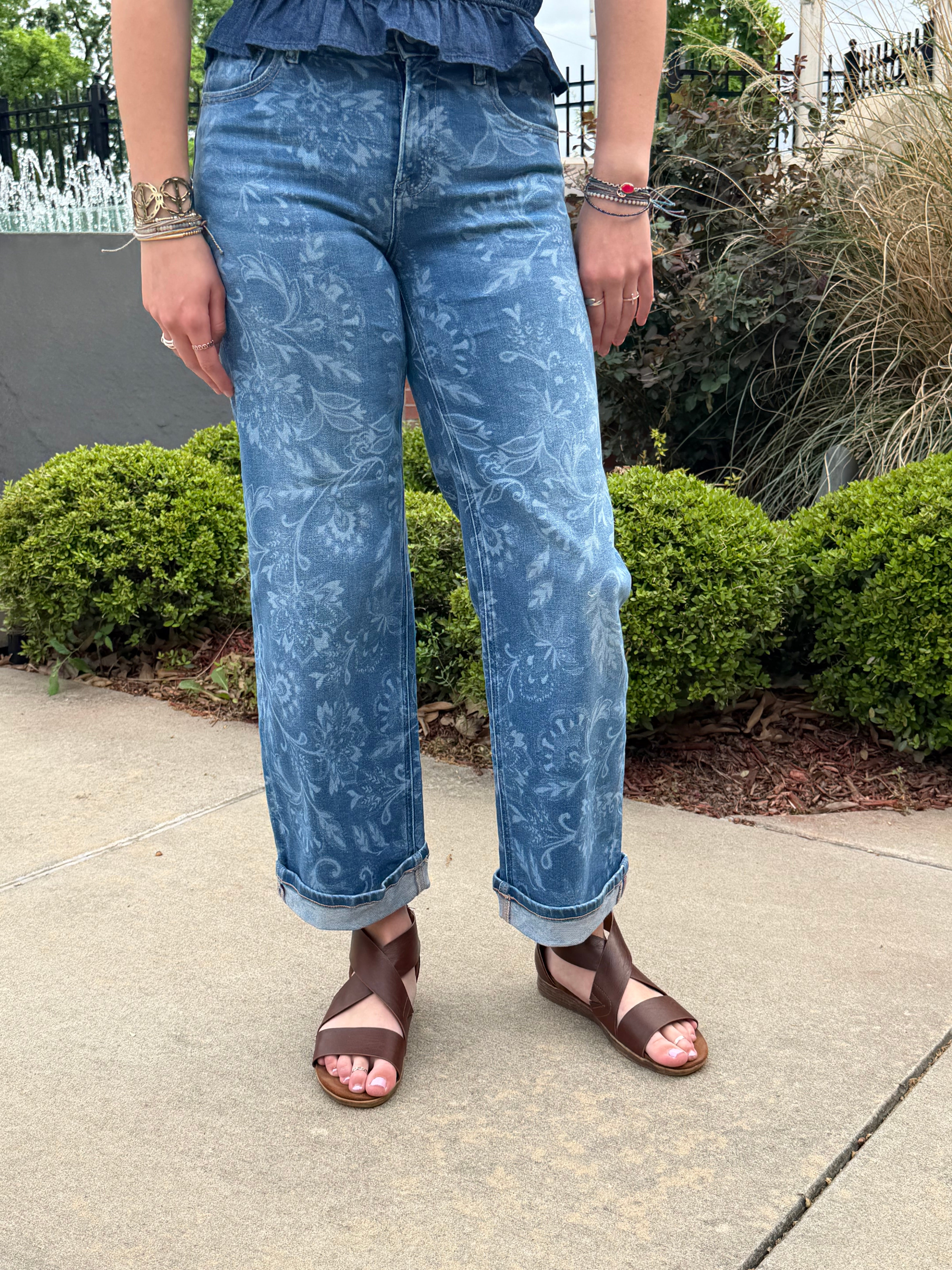Person wearing blue patterned pants and sandals on a sidewalk.