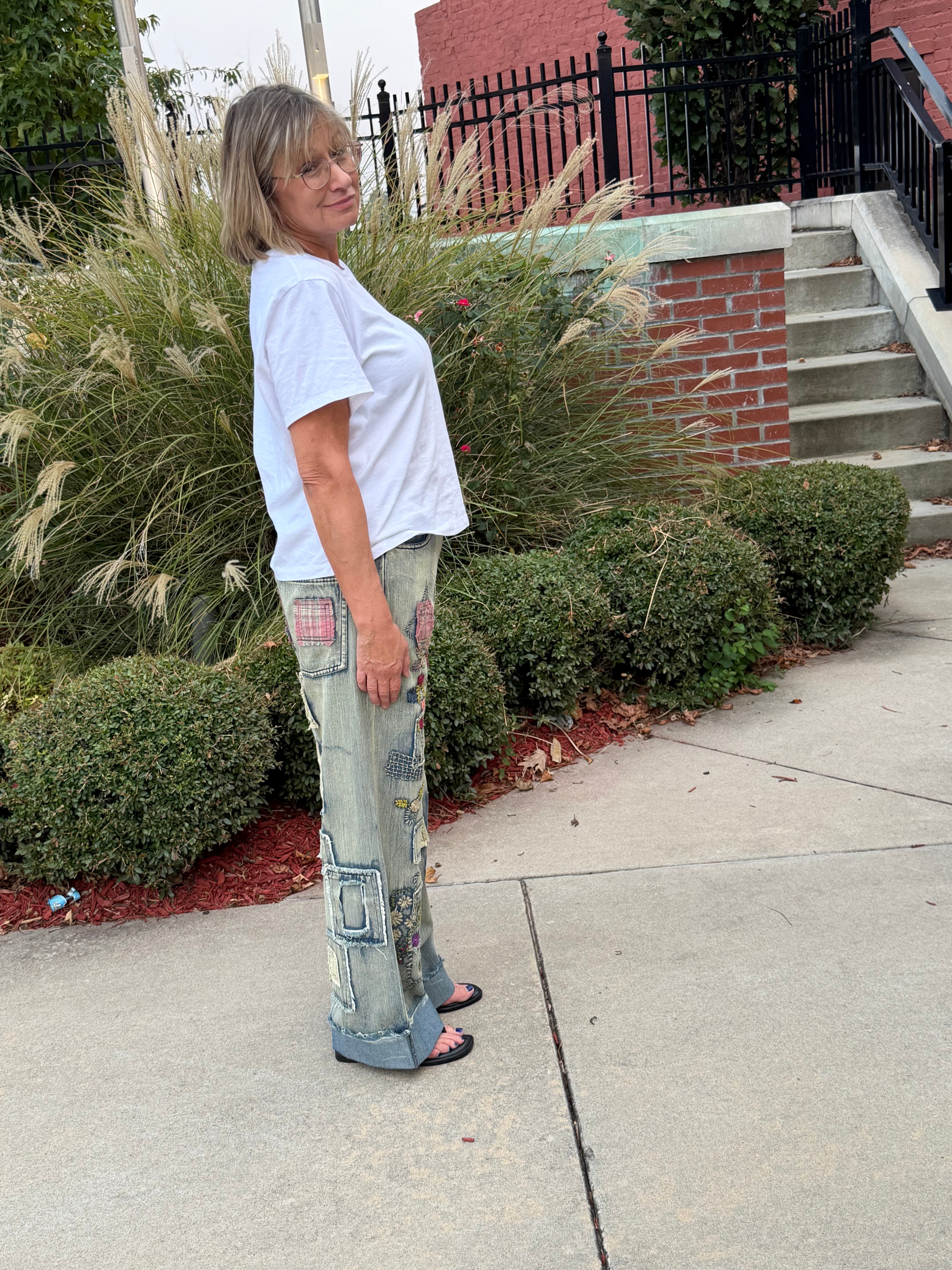 Side profile view of woman wearing Blue Velvet patchwork embroidered wide leg denim jeans showing cuffed hem and mixed-fabric patch placement
