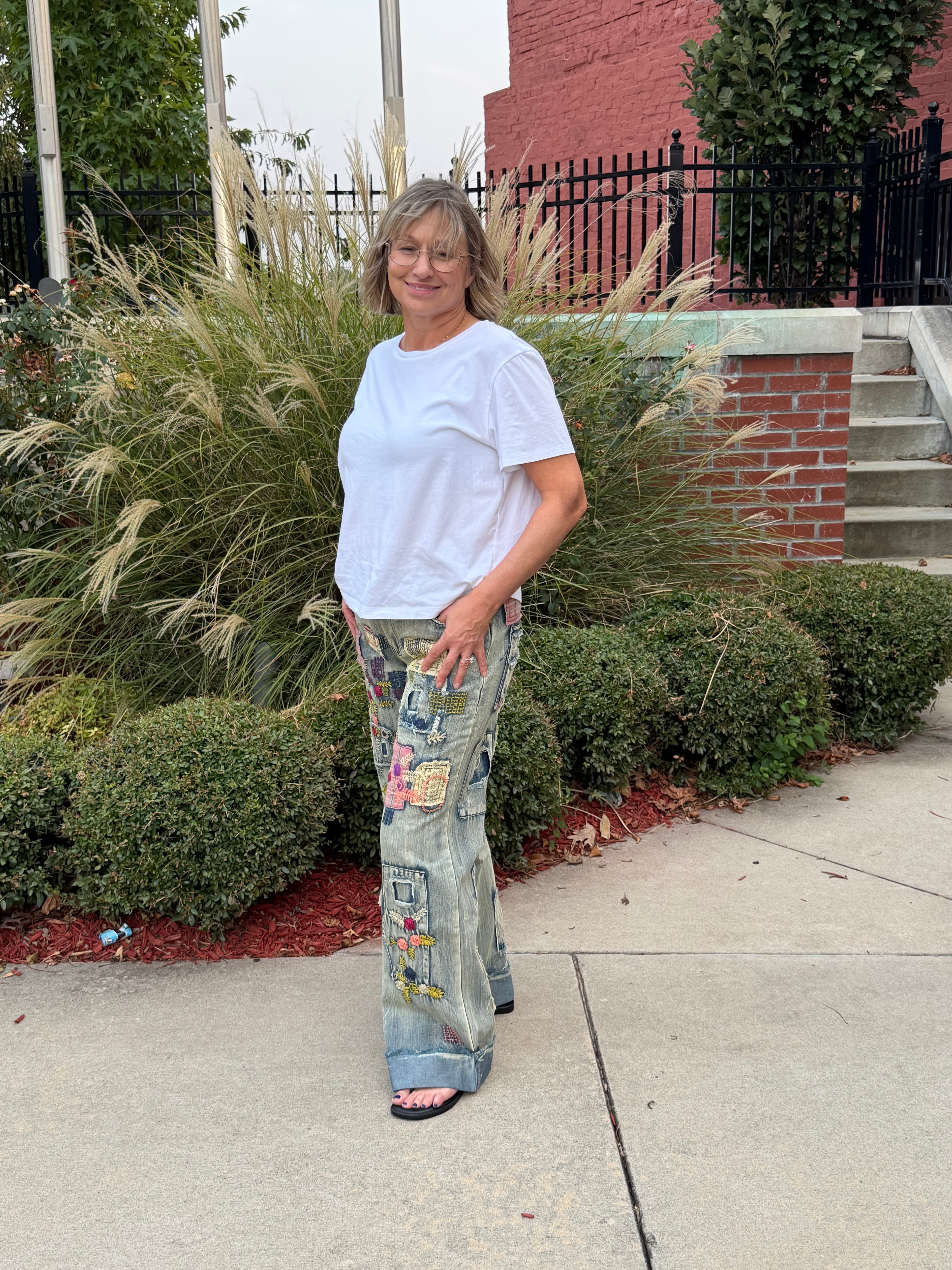 Side profile view of woman wearing Blue Velvet patchwork embroidered wide leg denim jeans showing cuffed hem and mixed-fabric patch placement