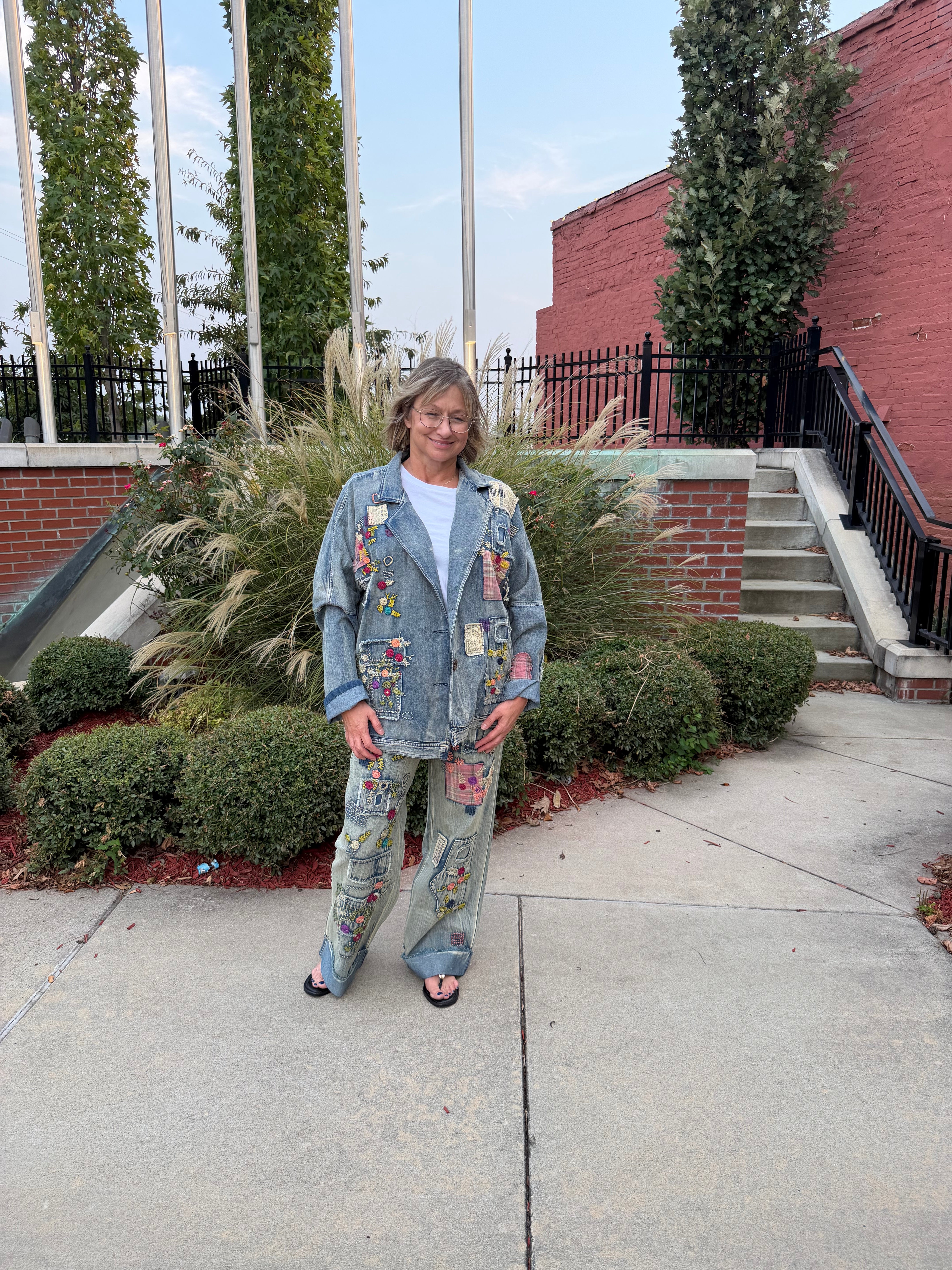 Front view of woman wearing Blue Velvet artisan patchwork embroidered denim jeans styled with matching patchwork denim jacket, full length outdoor shot