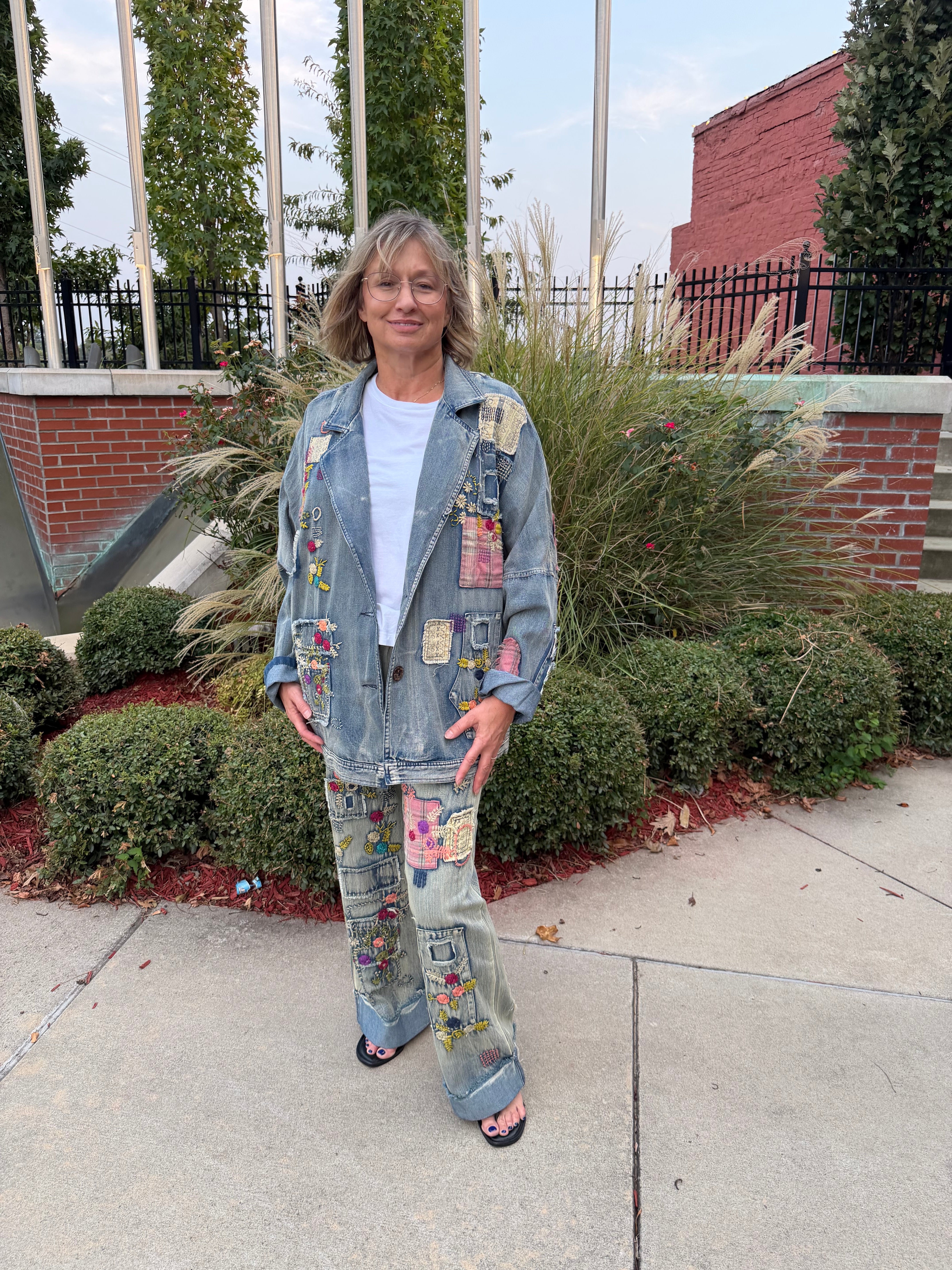 Front view of woman smiling wearing Blue Velvet patchwork embroidered denim jeans with matching patchwork jacket, hands in pockets
