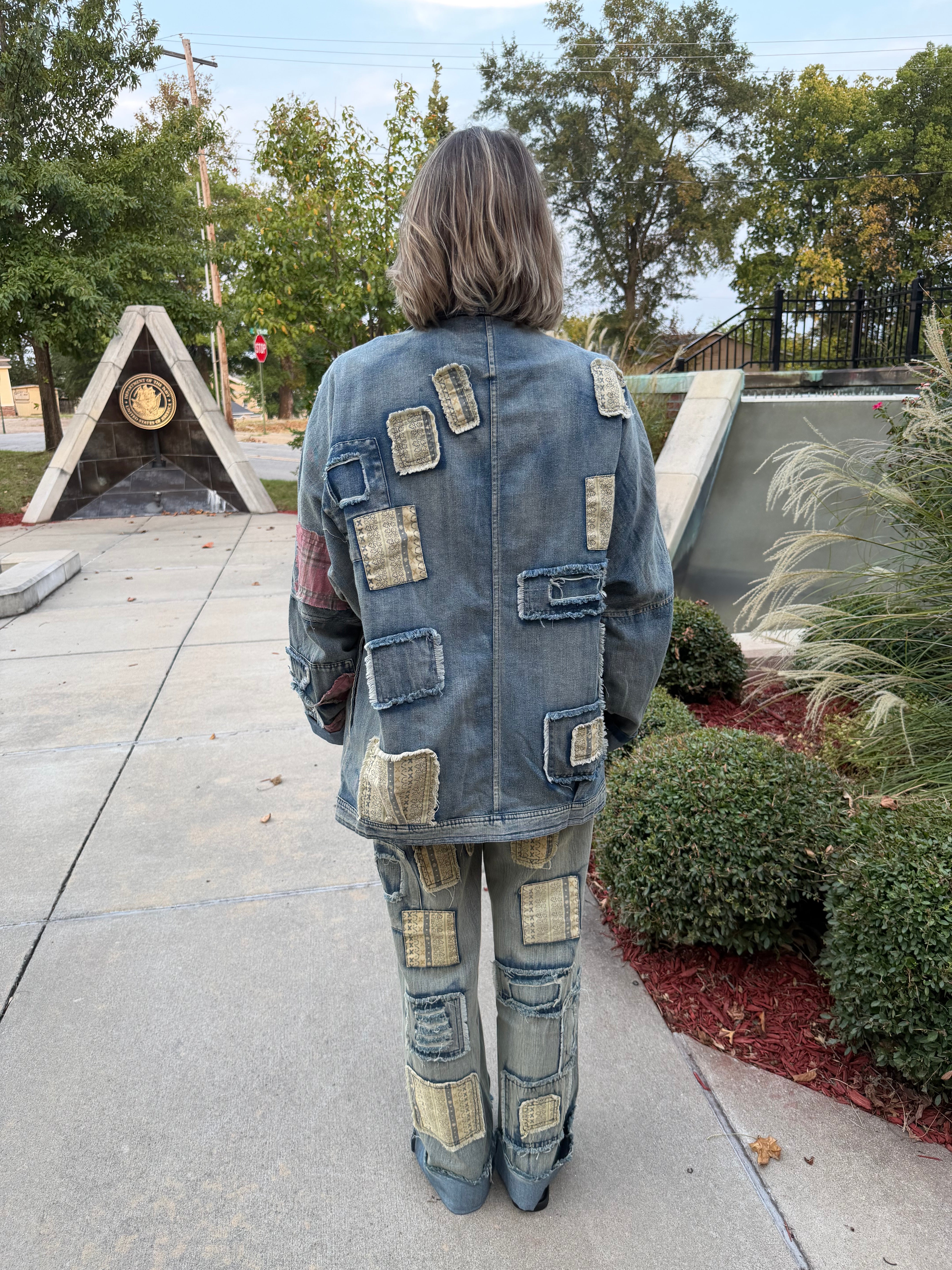Back three-quarter view of woman in BlueVelvet artisan patchwork denim jeans and jacket showing cuffed hem and layered patch detail
