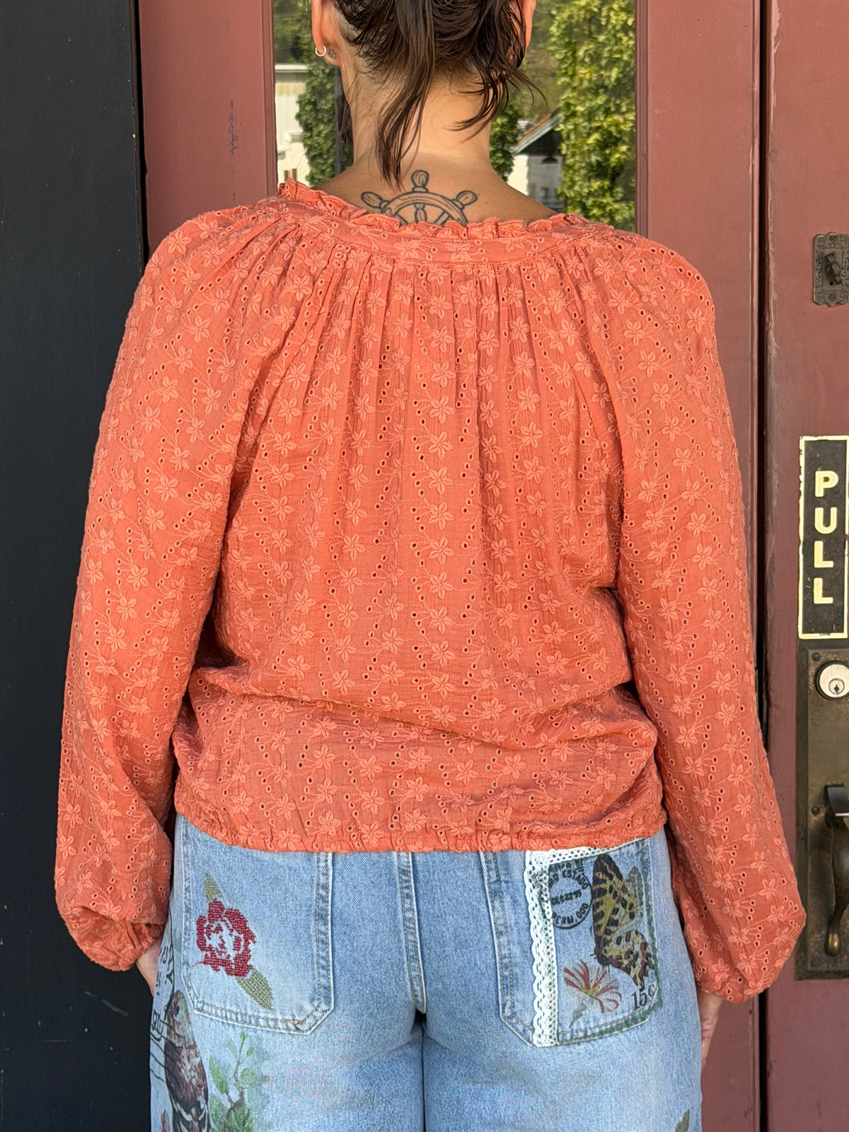 Woman in a terracotta floral eyelet blouse, back close-up showing gathered yoke and eyelet fabric detail